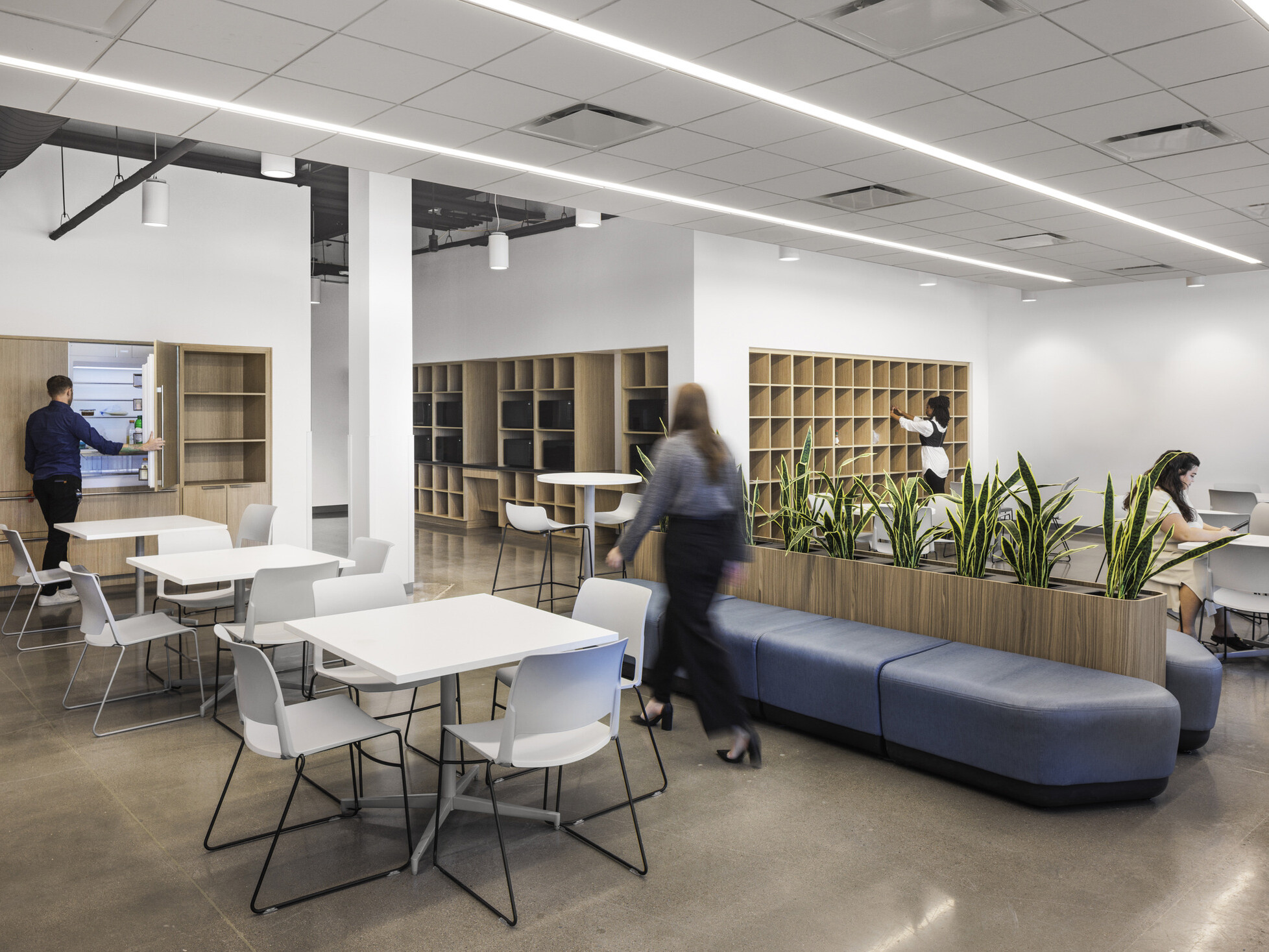 Sub-Zero Group employee break room; mix of standard and standing-height tables throughout; refrigerators clad in wood paneling blending seamlessly into the wall; open cubby storage
