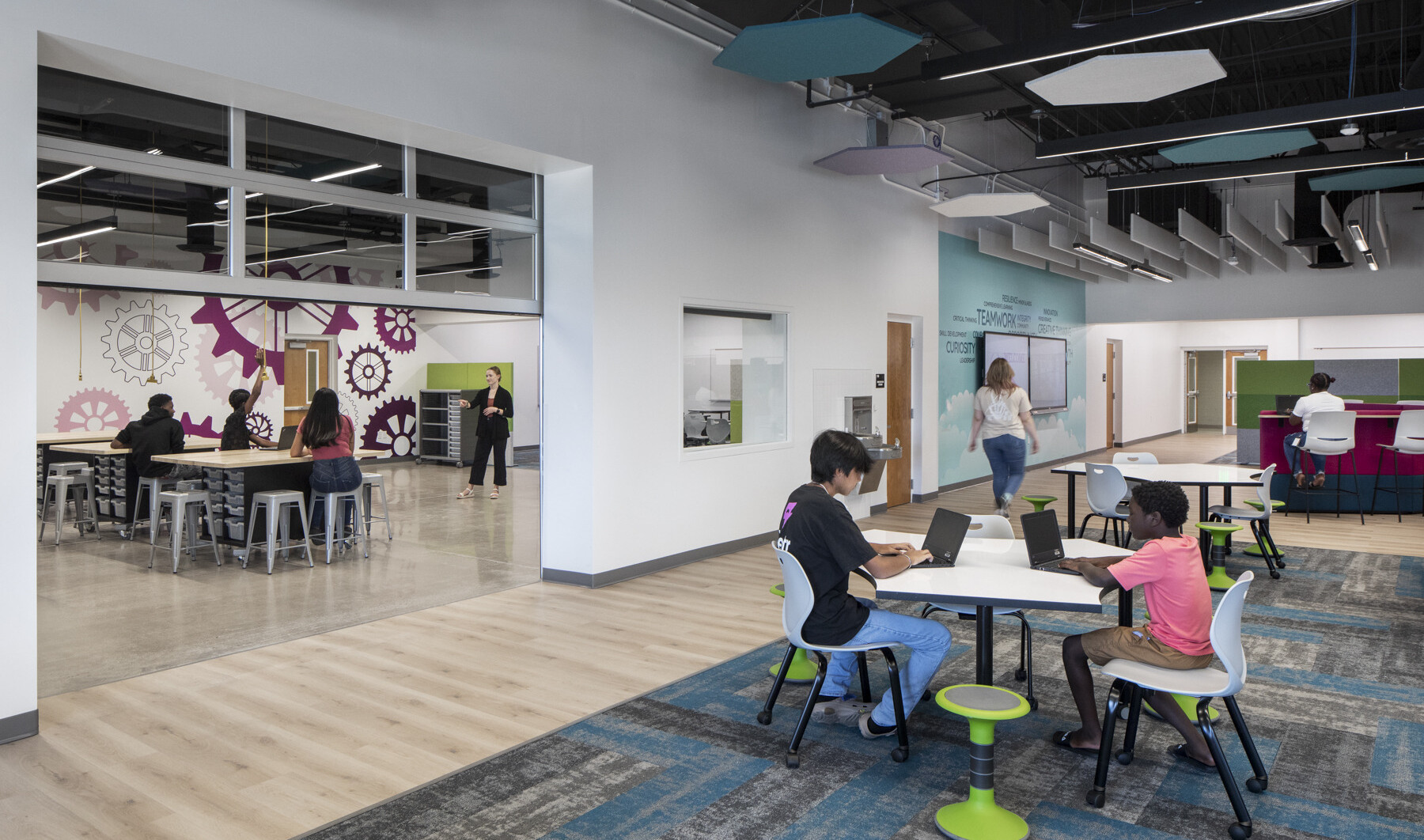 Open learning space inside a school with white walls, modern carpet and furniture, and an roll up door that is open looking inside a classroom