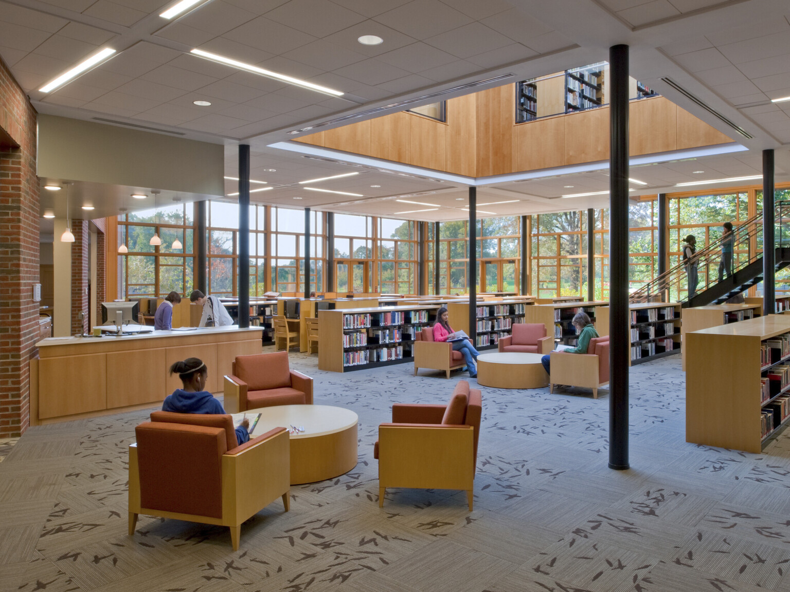 Double height glass facade library, armchair seating area, half height shelves, atrium around stairs to 2nd floor, interior windows