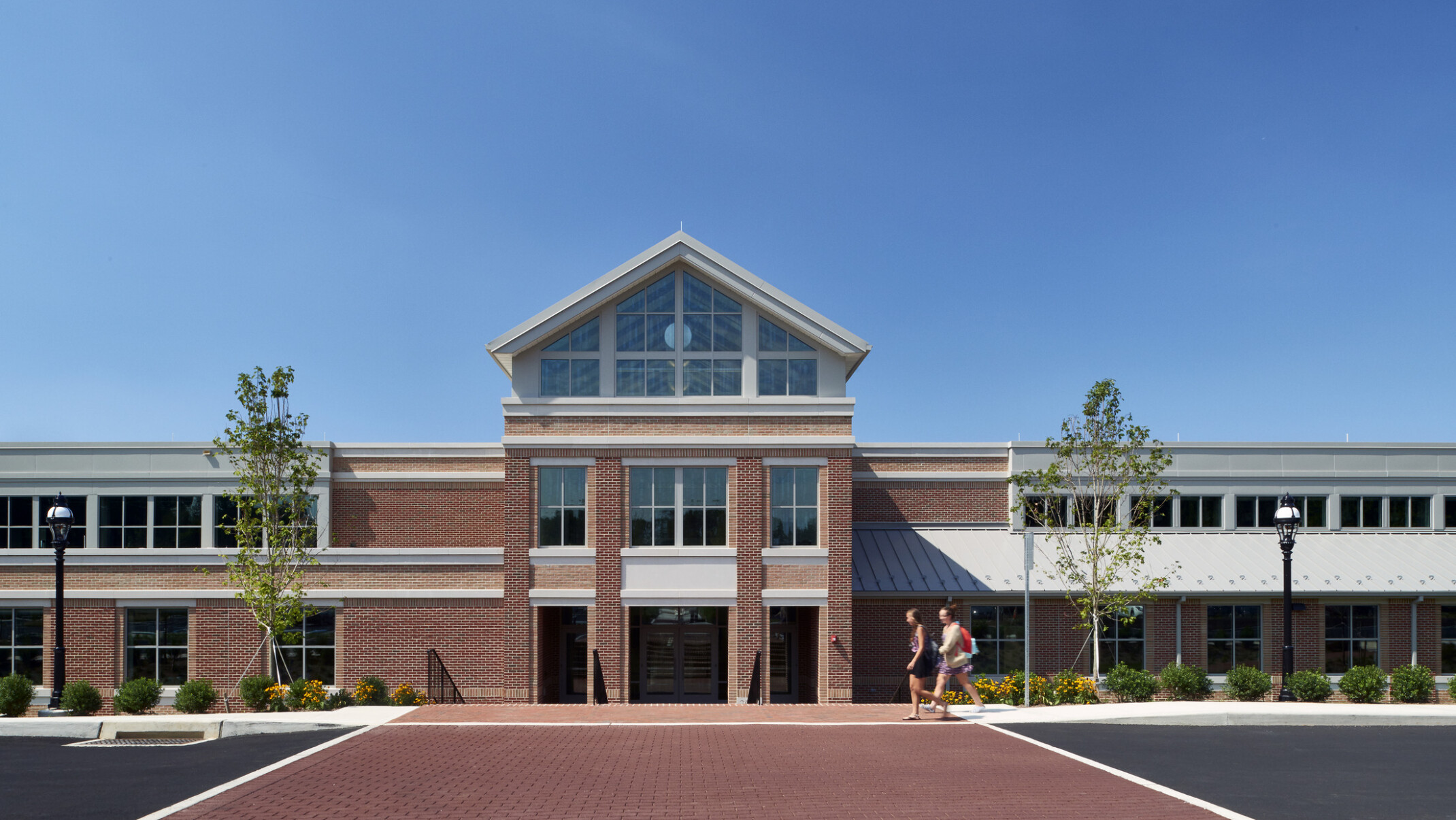 Exterior of a red brick two-story building with a high peak outlined in white filled with windows