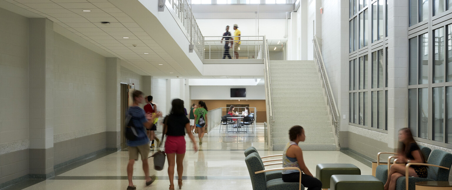 Multistory hallway looking at a seating area in front of a white staircase filled with high school students