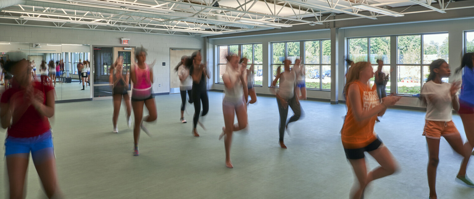 High school dance room lined with windows and a mirrored back wall filled with students