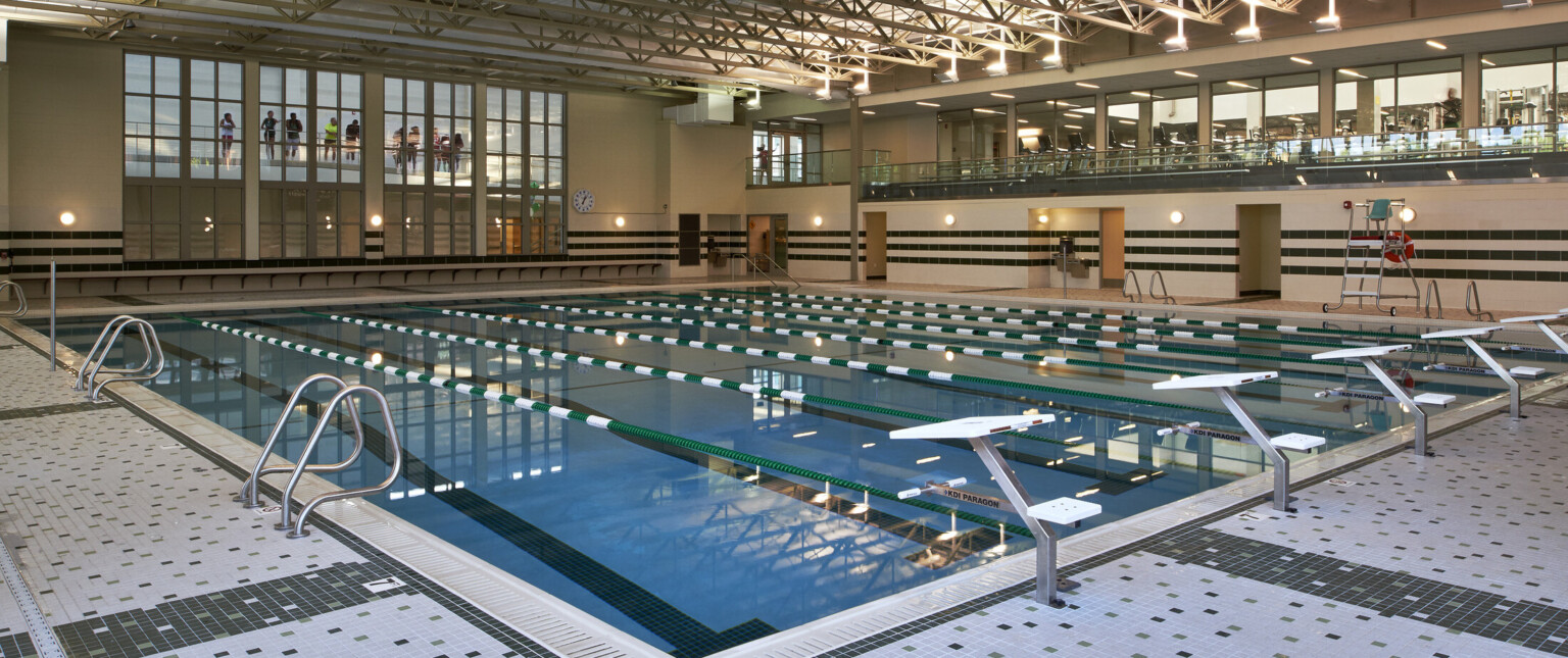 Multistory high school natatorium with a second story gym overlooking a blue swimming pool