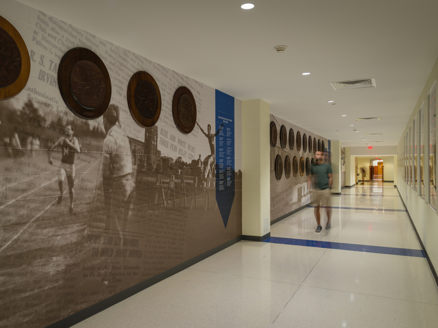 Hallway with murals to the left and round art pieces hung on top, white flooring with blue accents