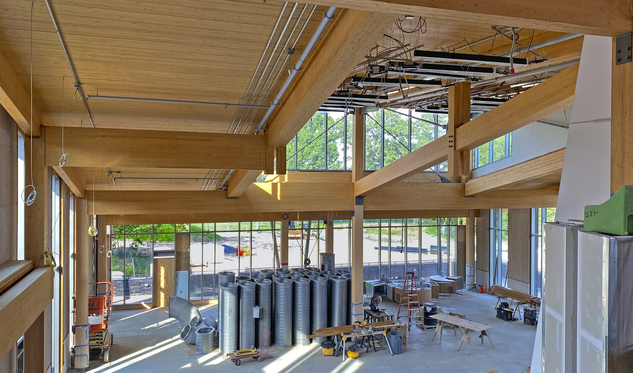 Dining commons interior under construction looking from upper level. Mass timber walls and ceiling, equipment and large windows