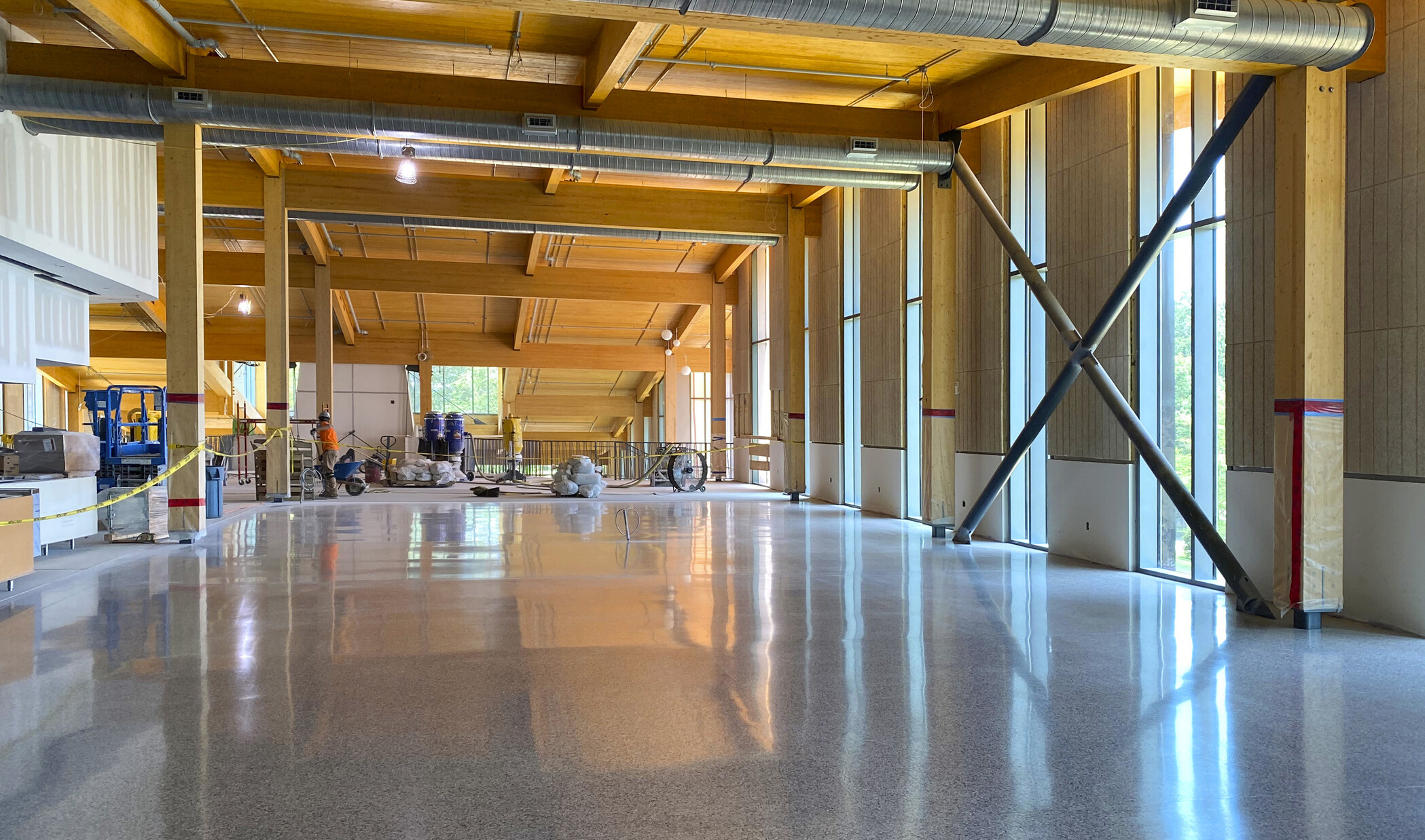 Dining commons interior under construction. Mass timber walls and ceiling exposed with ductwork and large windows