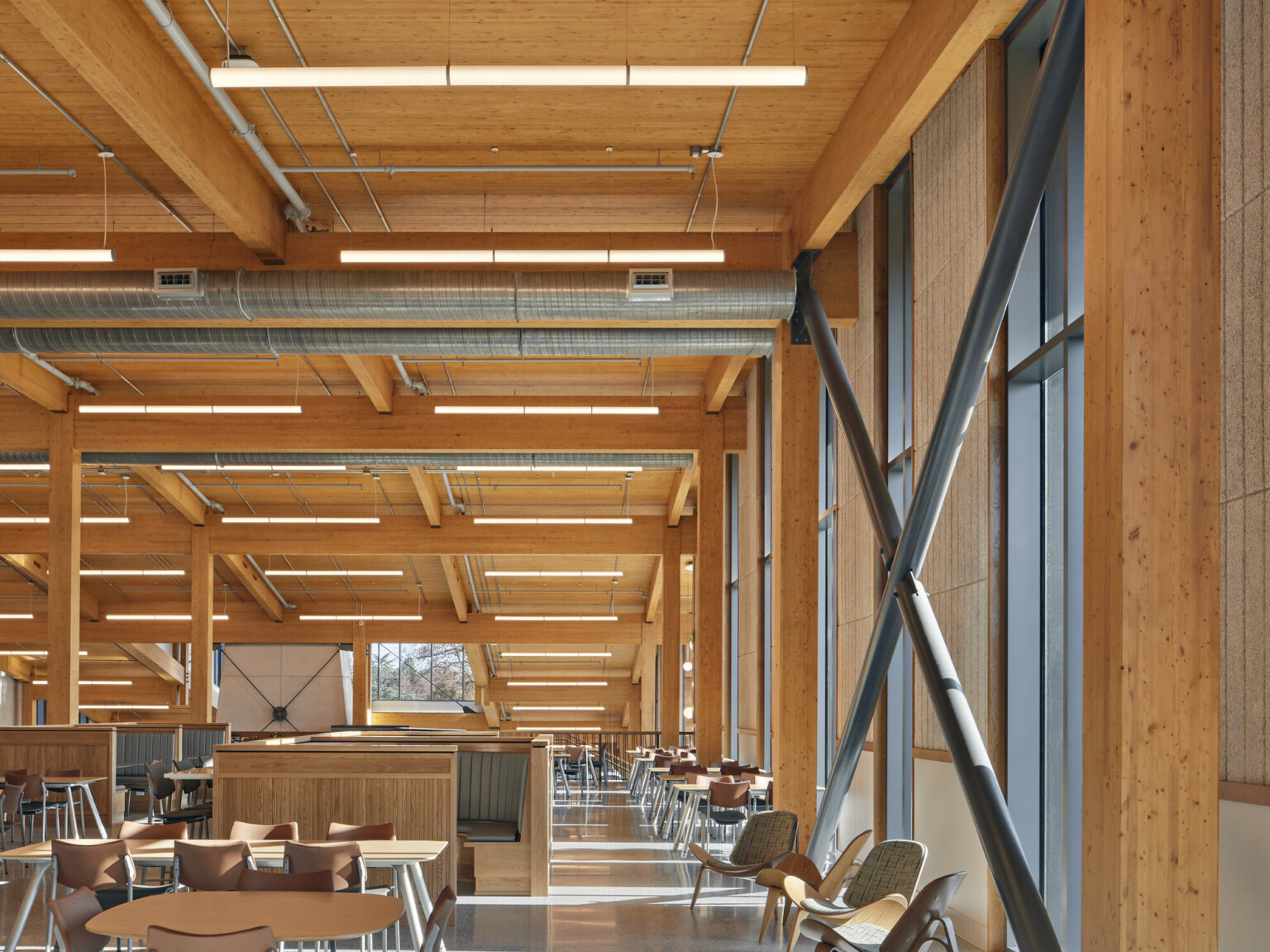 mass timber triple-height ceilings and stone walls, overhead energy-efficient low-wattage lighting, exposed ducting, steel supports, floor-to-ceiling windows provide natural light, wood and steel seating