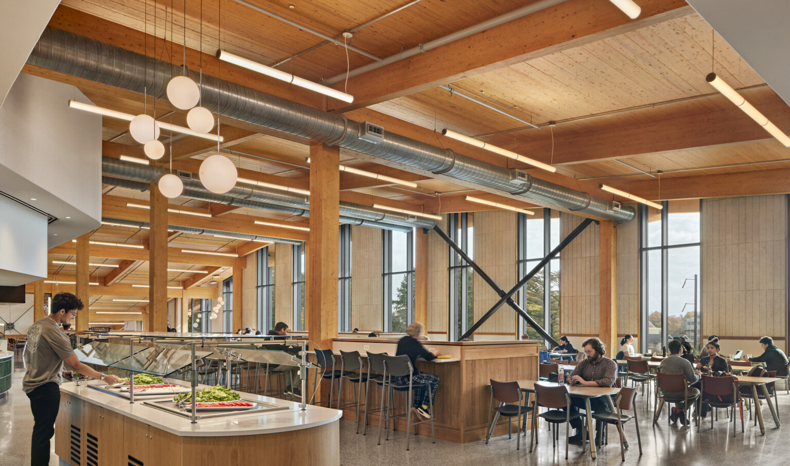 Dining area with flexible seating below wood ceiling with beam details, hanging rod lights, fireplace with white chimney back