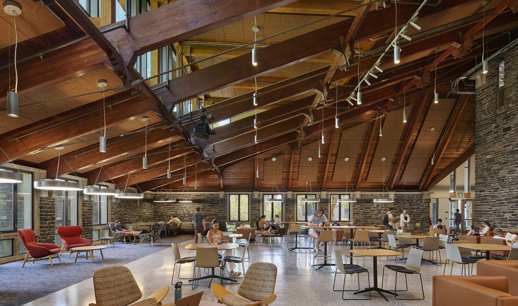 College common area filled with seating, exposed beams in the ceiling, and surrounded by exposed rock walls