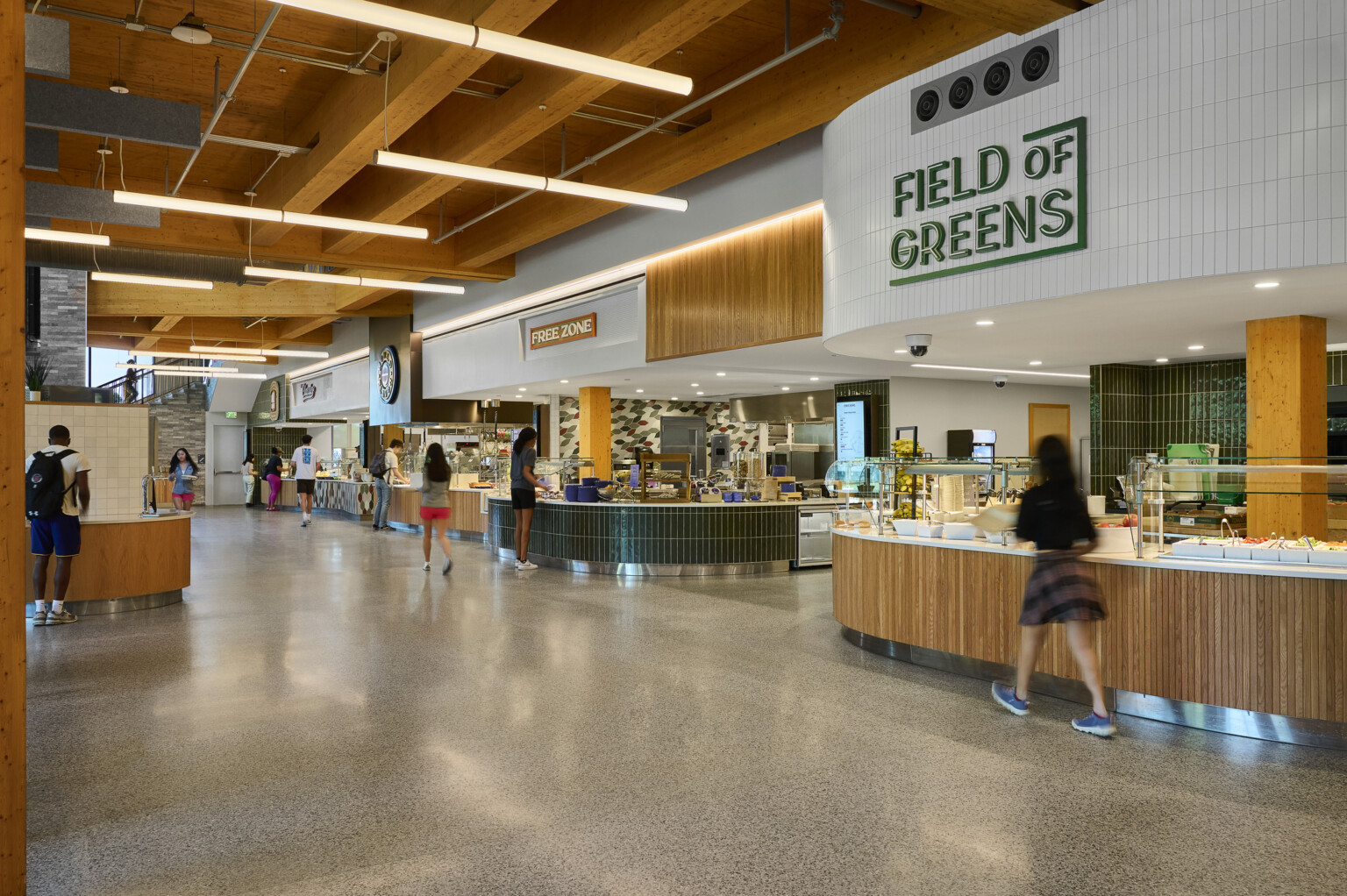 College dining hall with tall ceilings, exposed mass timber wood ceiling, green and white tile accents, raw concrete floors