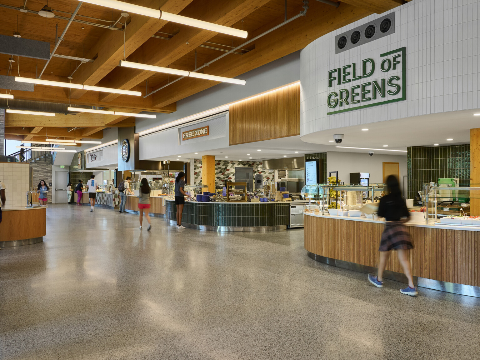 College dining hall with tall ceilings, exposed mass timber wood ceiling, green and white tile accents, raw concrete floors