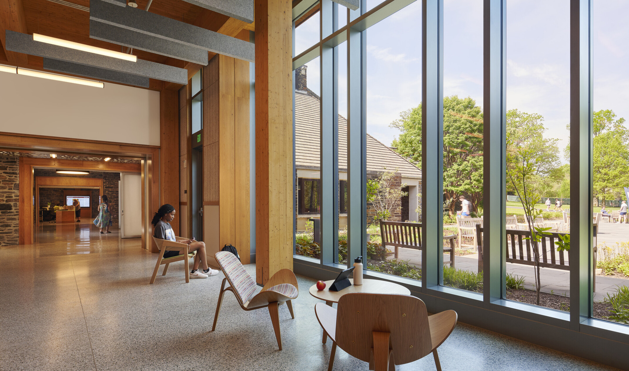seating area in Swarthmore College Community Commons and Dining hall; lounge chairs in a timber building facing a floor to ceiling windows to green garden space