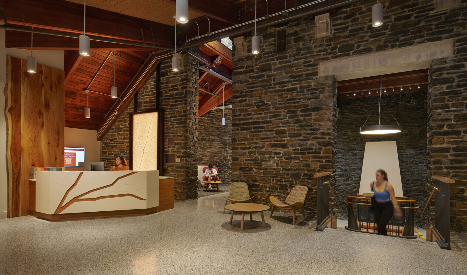 Interior common space with reception desk, exposed mass timber accent walls and ceiling, rock stone walls, pendant lights
