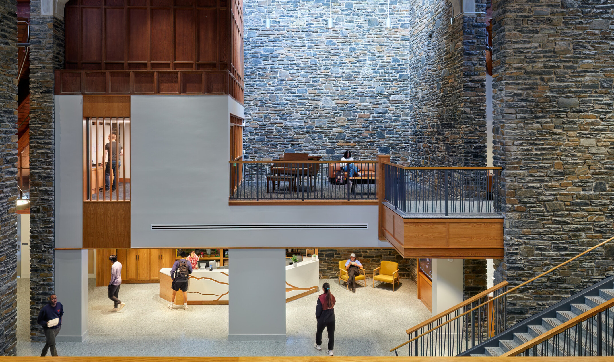 Interior triple height atrium with stone walls, large windows, lots of natural lights, mass timber exposed wood accents, looking across open space, views to first floor and opposite side of hall