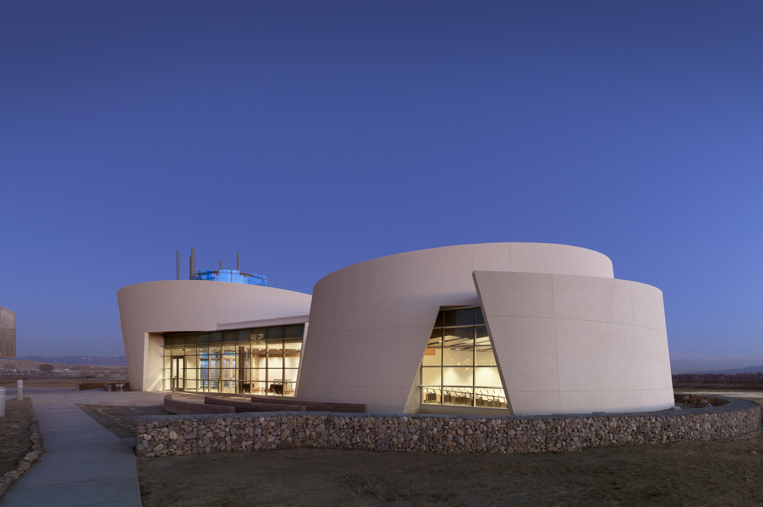 community and culture at dine college library, desert structure with an iconic design. Curved structure overlays itself and lit up from within with warm lights; dlr group design community and culture at dine college library, desert structure with an iconic design. Curved structure overlays itself and lit up from within with warm lights; dlr group design