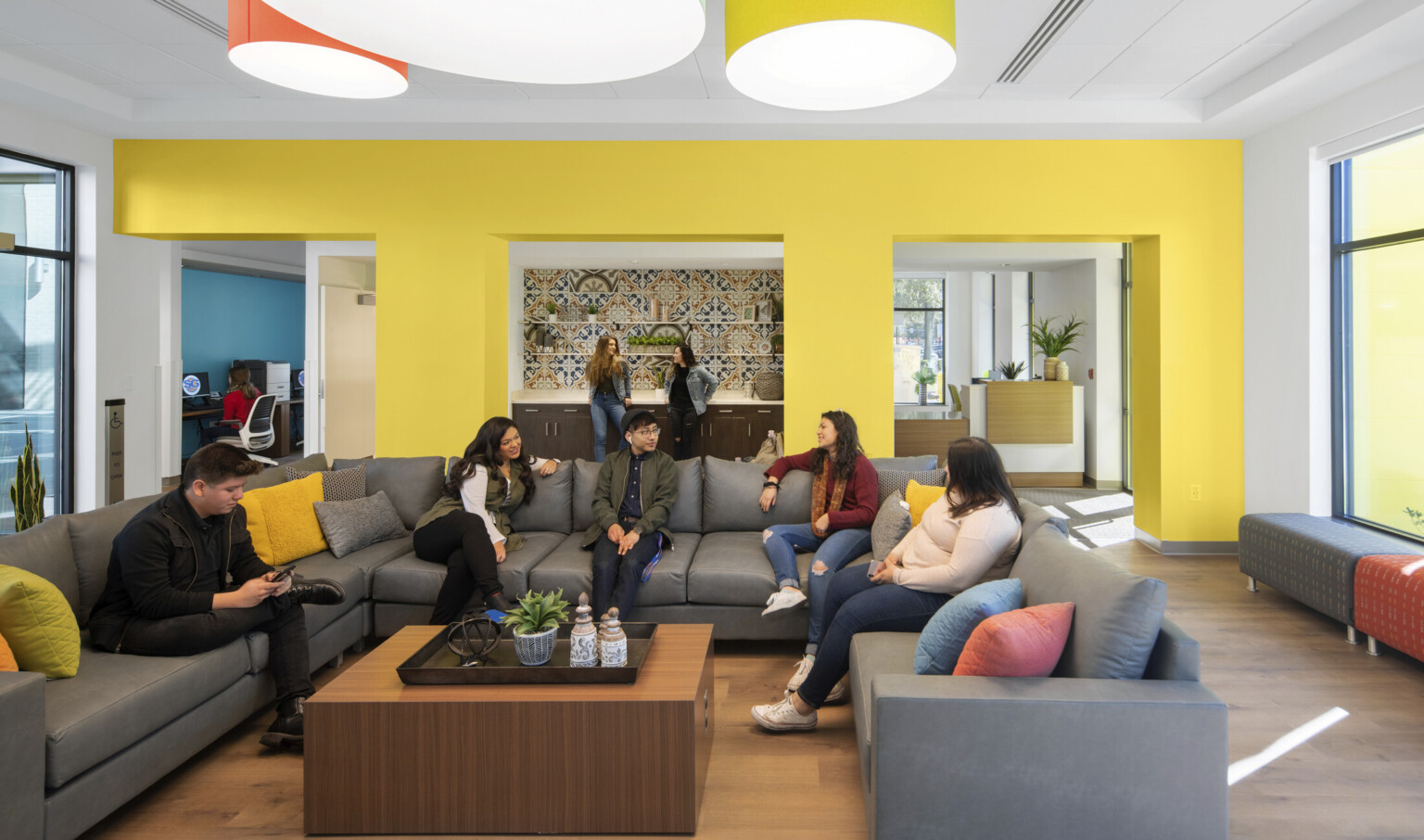 Yellow seating area off entry with large U shaped sectional and coffee table. Recessed counter in center of wall with tiles