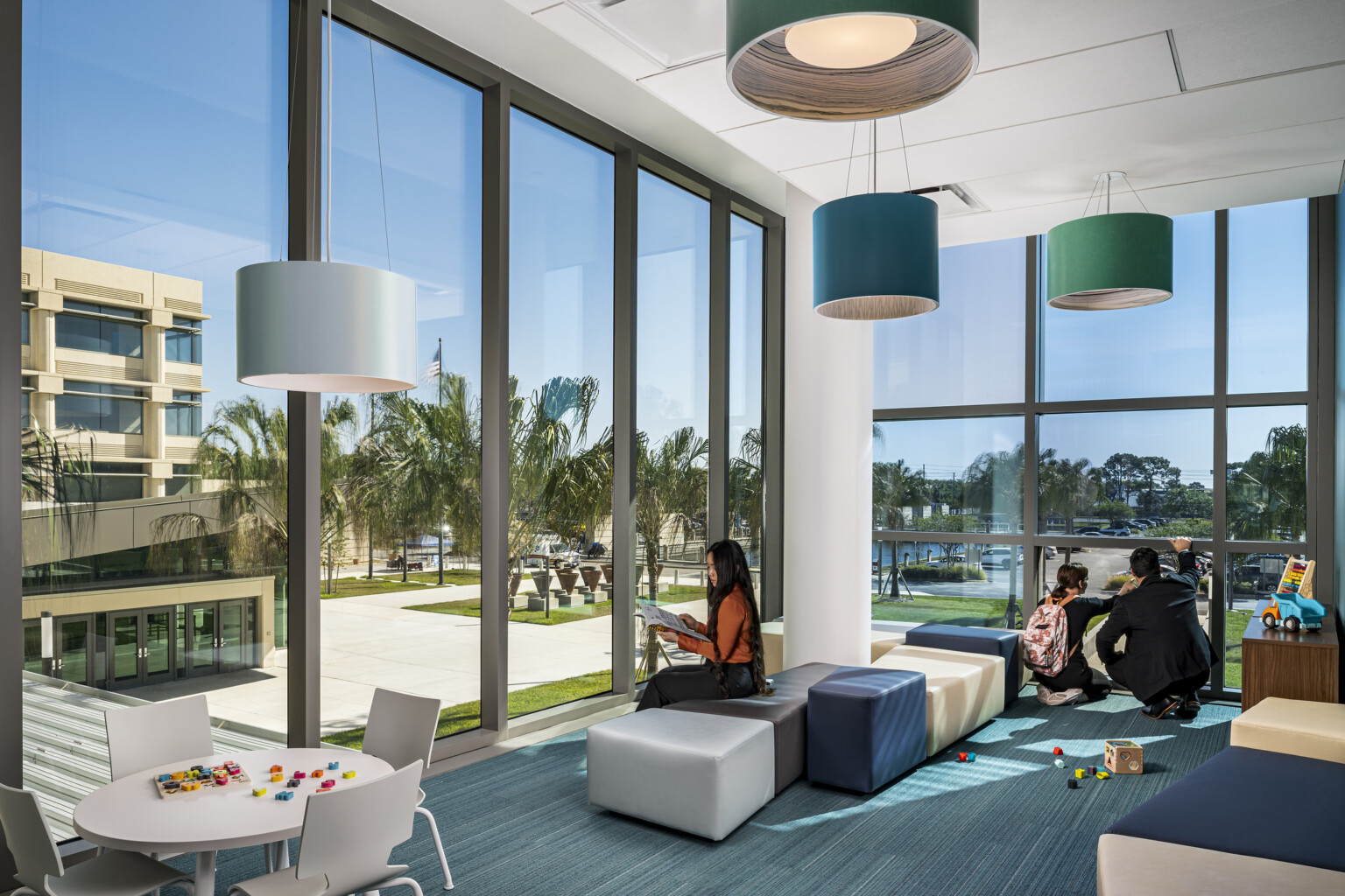 courthouse public area, high-ceilings, floor-to-ceiling windows fill all walls provide natural light, soothing blues and greens for flooring, modular seating areas, barrel lamps overhead with blue and green shades