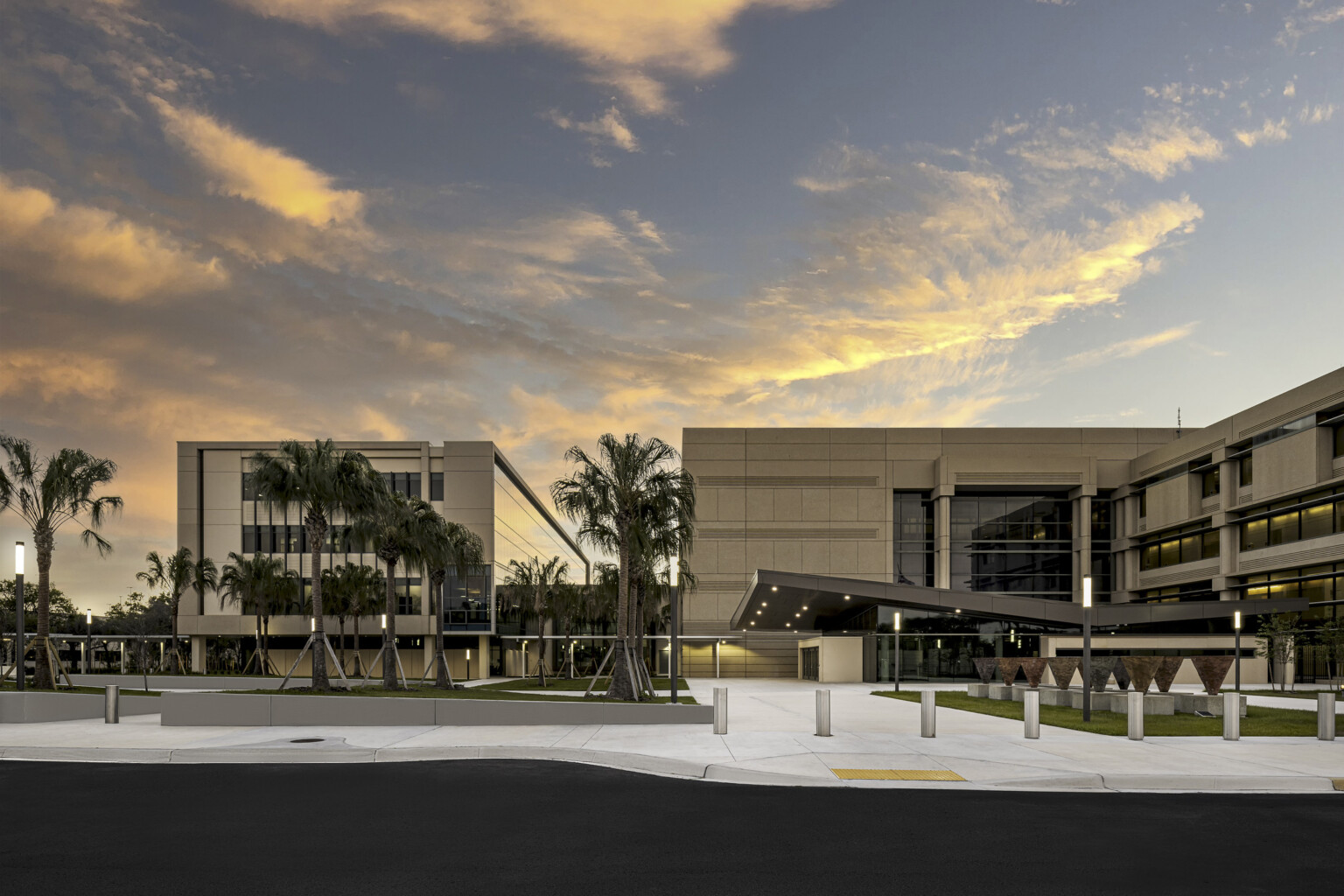 Two beige buildings attached with a breezeway at dusk with palm trees and ambient lighting