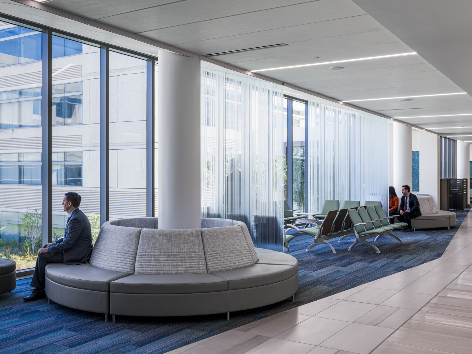 courthouse public area, high-ceilings, floor-to-ceiling windows provide natural light for well-being, natural wood and blue low-pile carpet, modern circular upholstered group seating