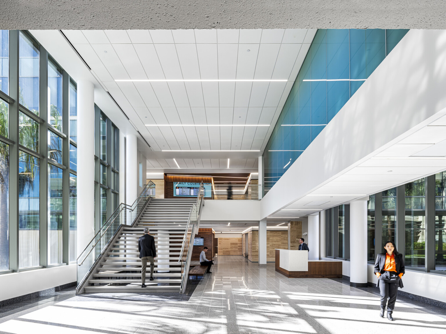 interior lobby with staircase, turquoise-tinted clerestory windows on one wall, darker wood panels on back wall, polished concrete flooring in soothing cool hue, floor-to-ceiling windows provide natural light