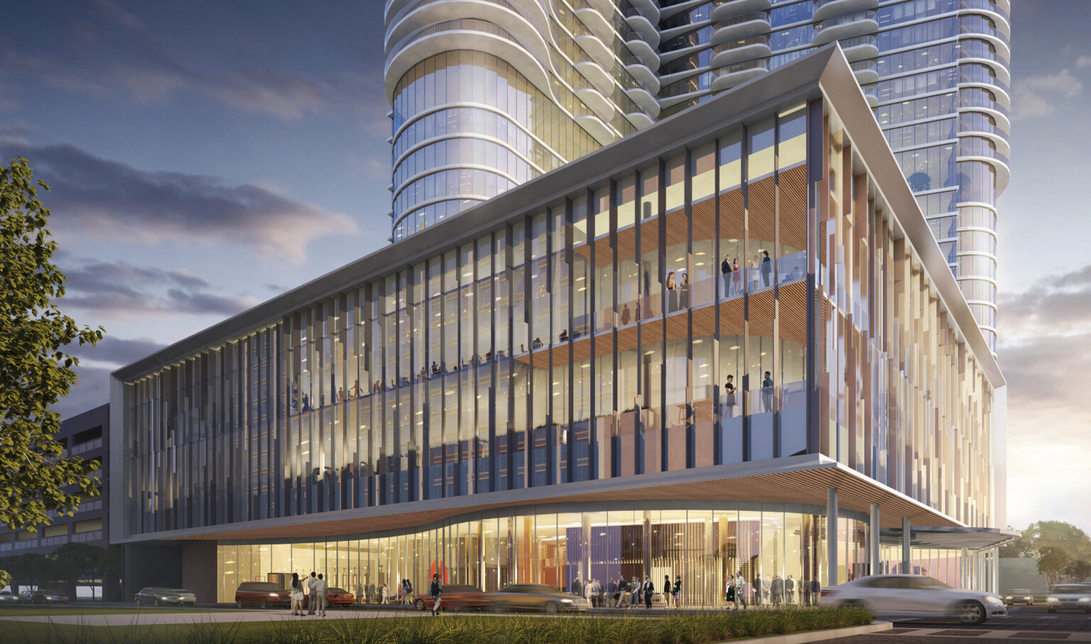 Lower building seen from corner, illuminated at night. Upper levels extend over curved 1st floor lobby. Building tower behind