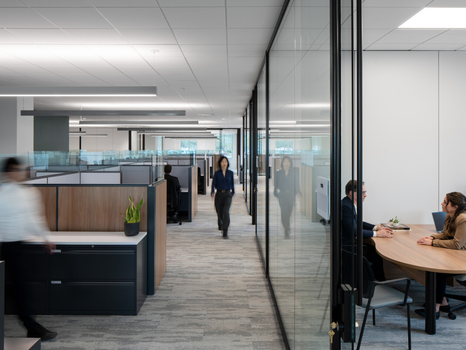 Interior of an office with glass offices surrounding open concept desks divided by partitions
