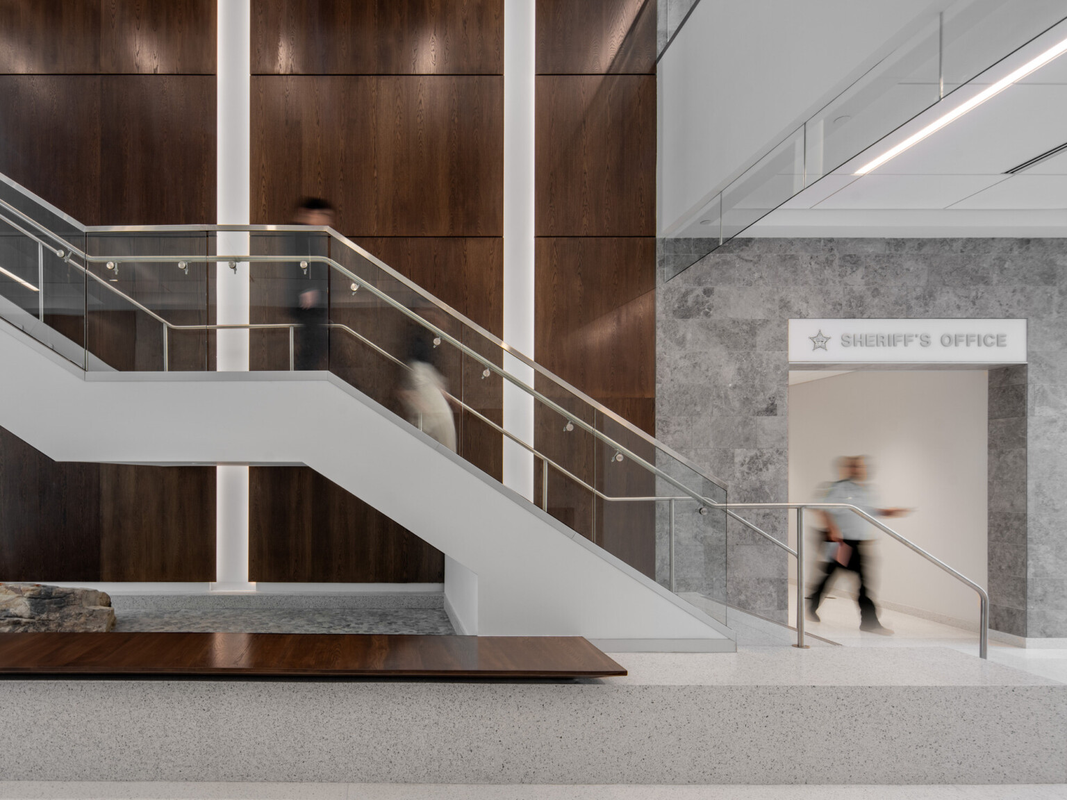 Office stairway with glass railing, wooden accent wall, with a grey marble inset with words Sheriffs Office