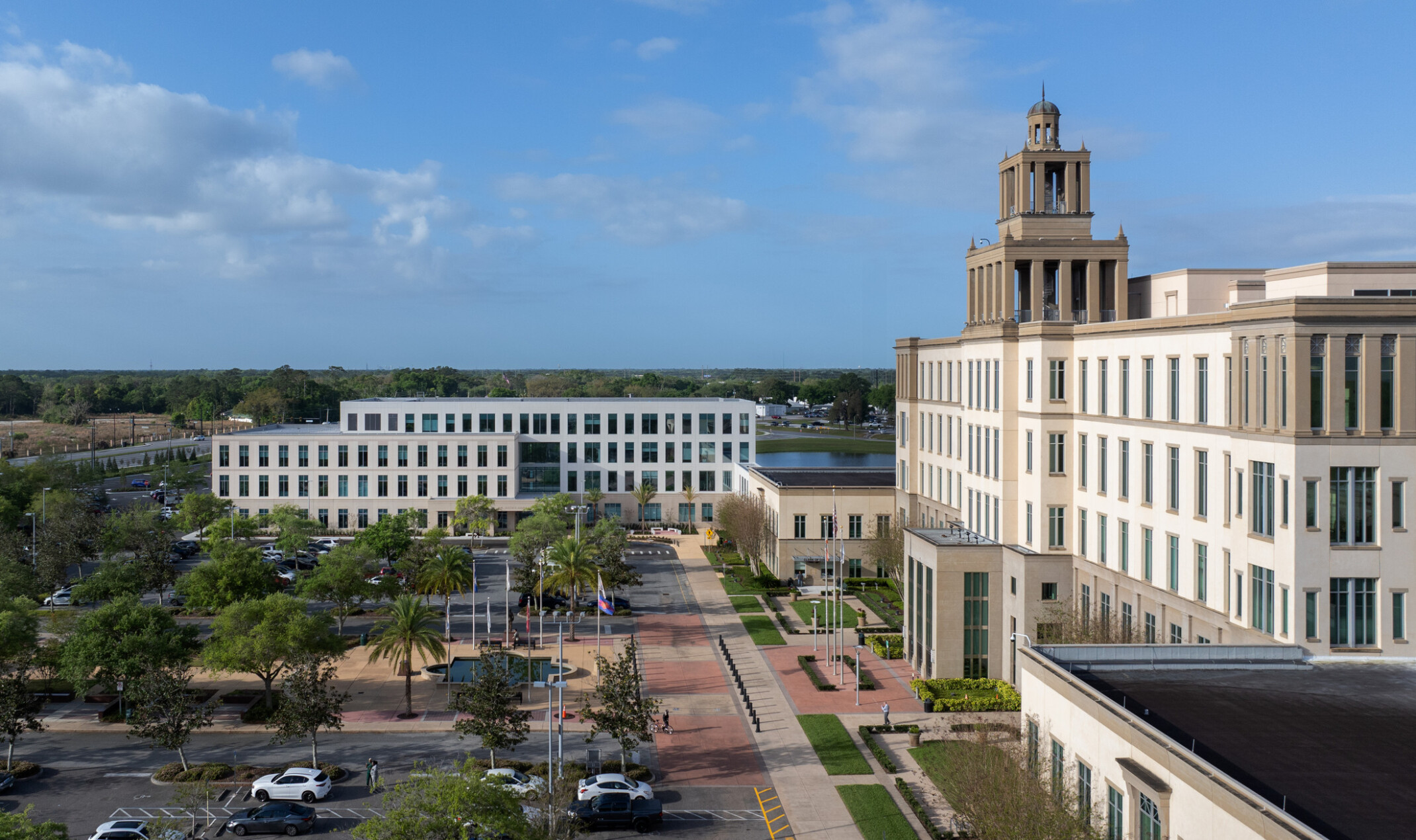 Large four-story courts building with three tiered cupola occupies the right side of the image. In the center and foreground, a parking lot and public plaza with fountain stand before a 4-story government building in front of a lake.
