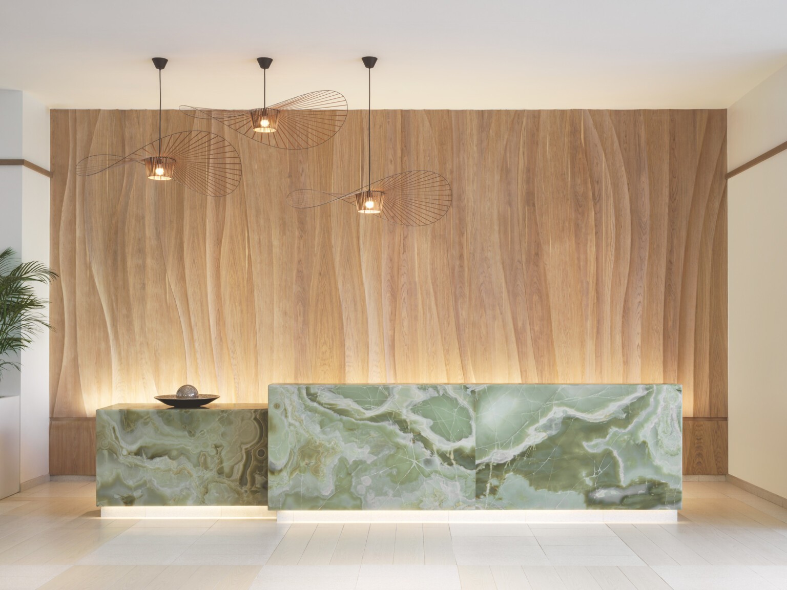 AC Hotel Naples 5th Avenue lobby showcasing a green jade desk in front of a natural wood wall with modern light fixtures suspended from the c