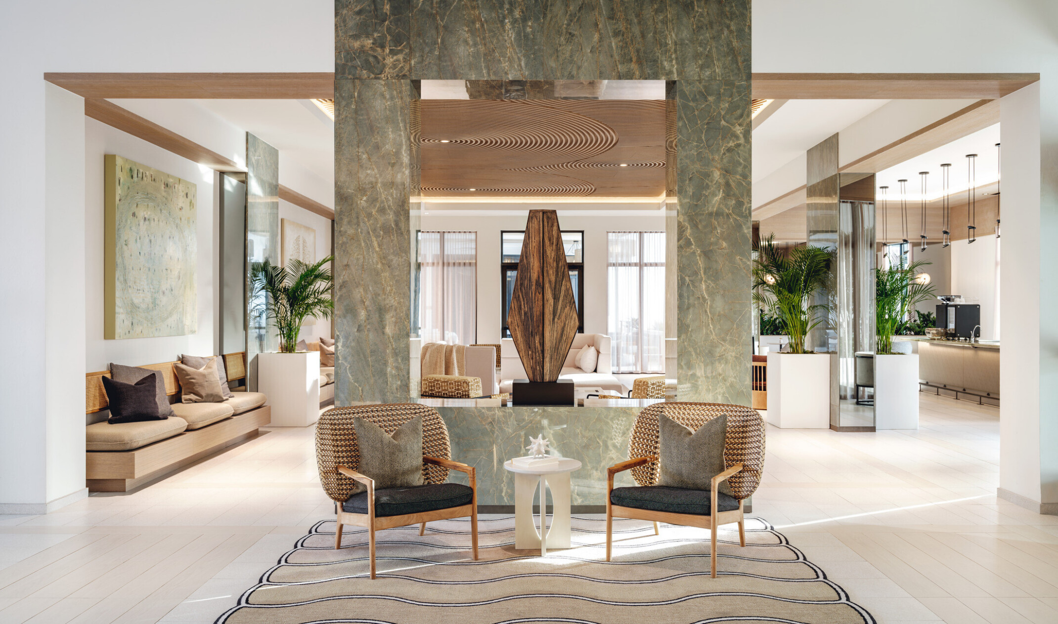 Hotel lobby lounge divided by a jade stone rectangle structure with cozy seating and coffee bar.