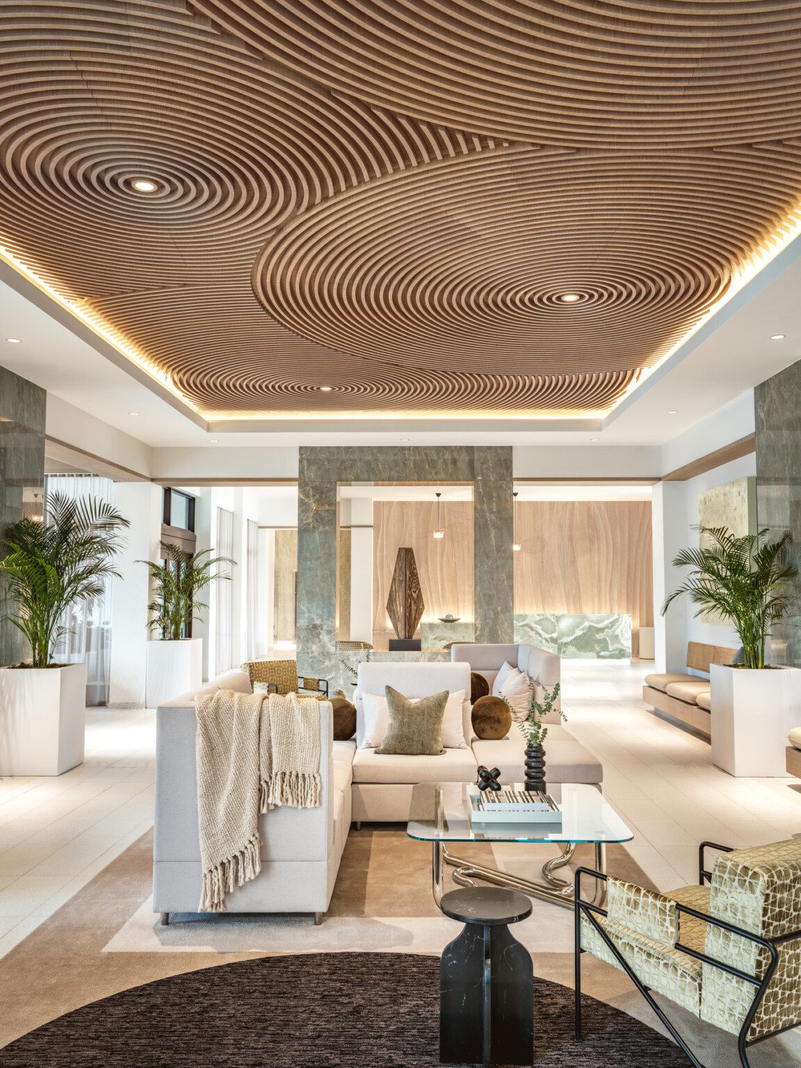 Modern hotel lobby with white couches on natural area rugs, natural wood ceilings, modern green marble sculpture