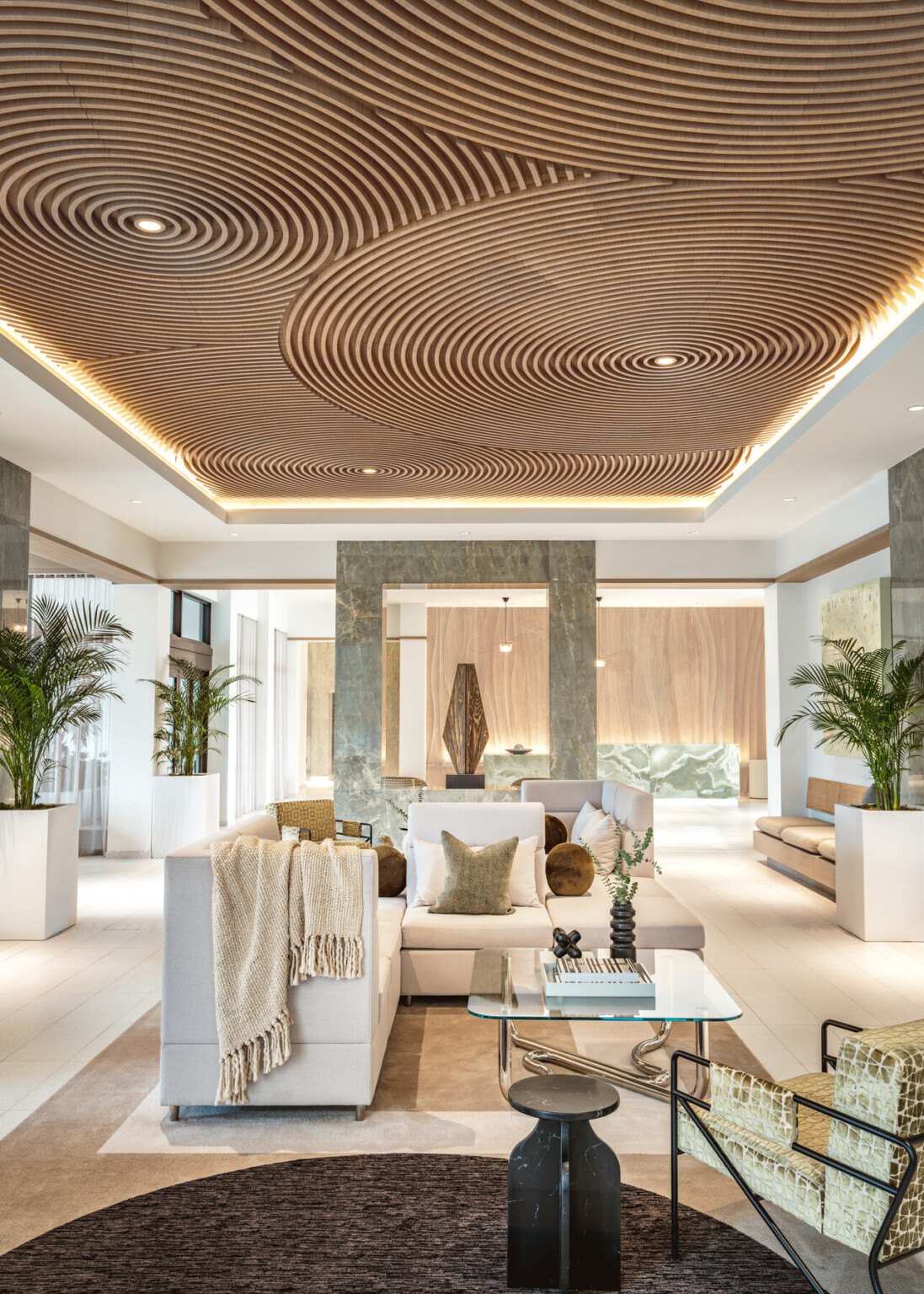 Modern hotel lobby with white couches in front of a green jade accent wall showcasing a sculpture