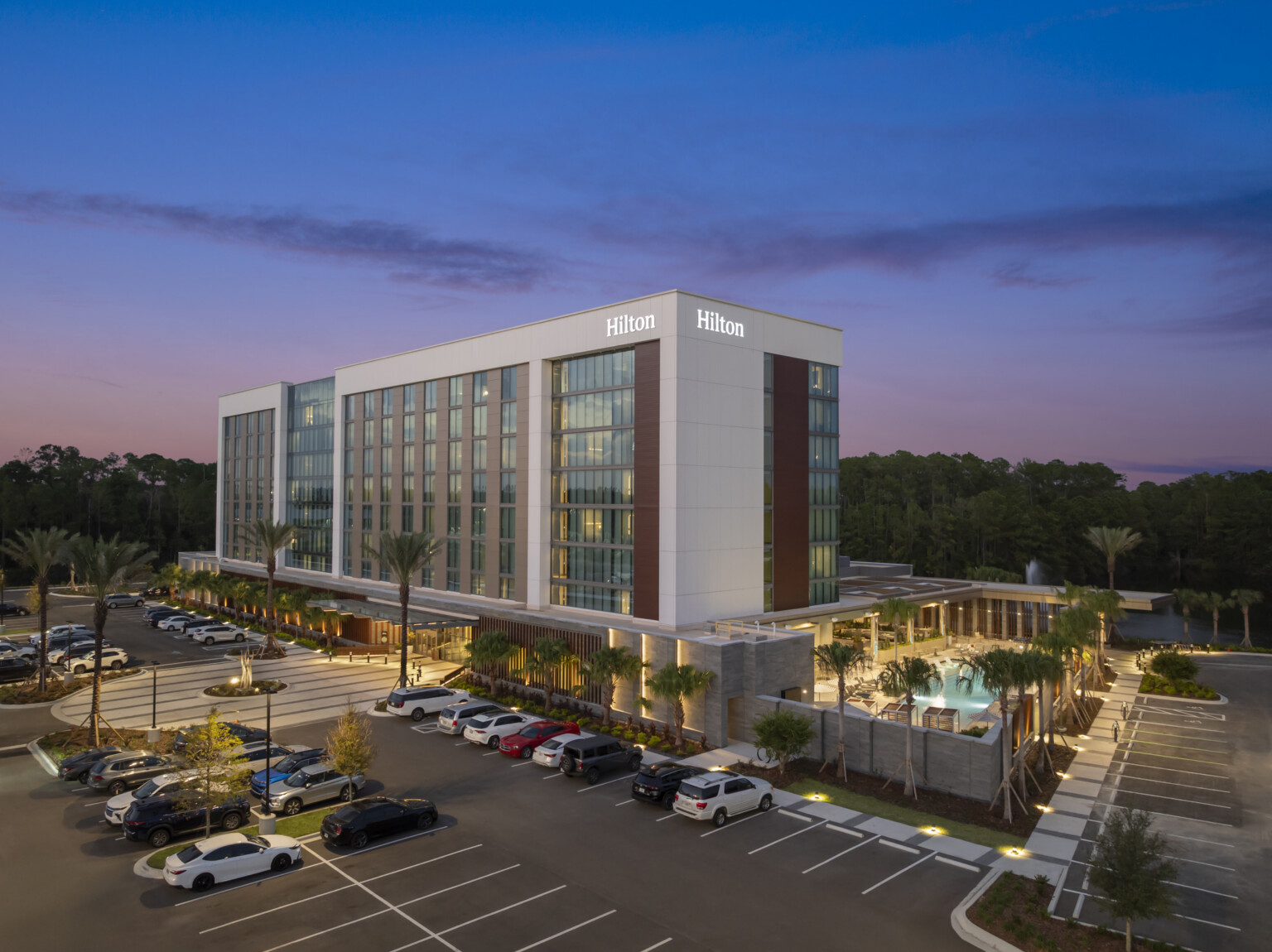 Front elevation of Hilton Jacksonville with glowing main entry and resort-style pool terrace, framed by simple architectural material detailing.