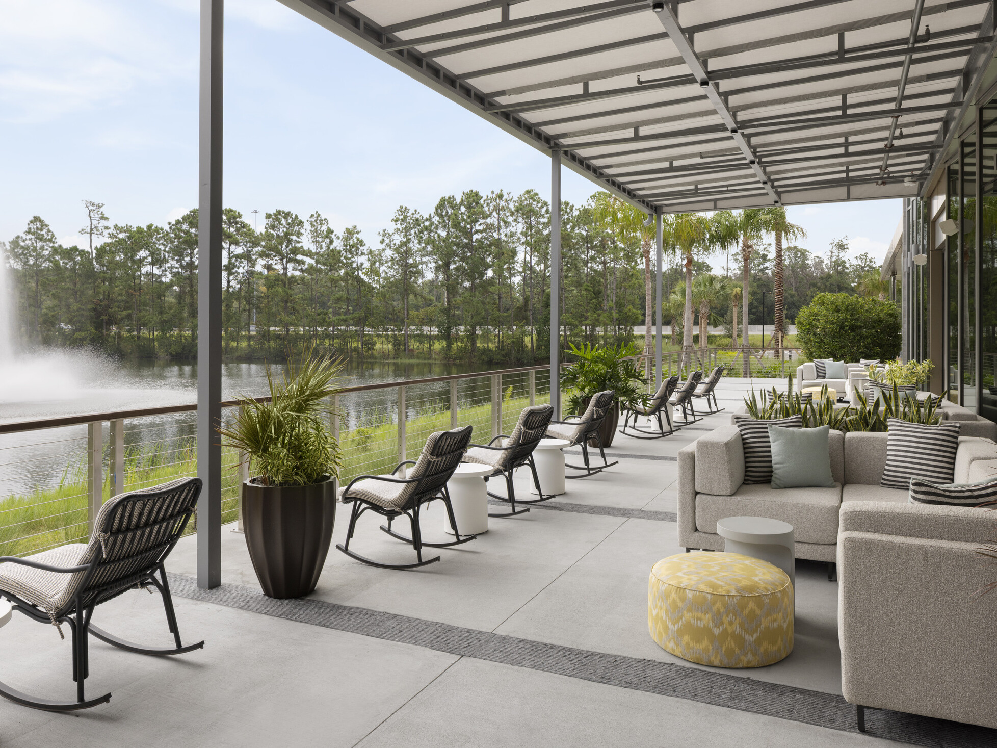 Covered outdoor seating at Hilton Jacksonville overlooking the main pond with central fountain, featuring rocking chairs and grouped lounge seating along the window line