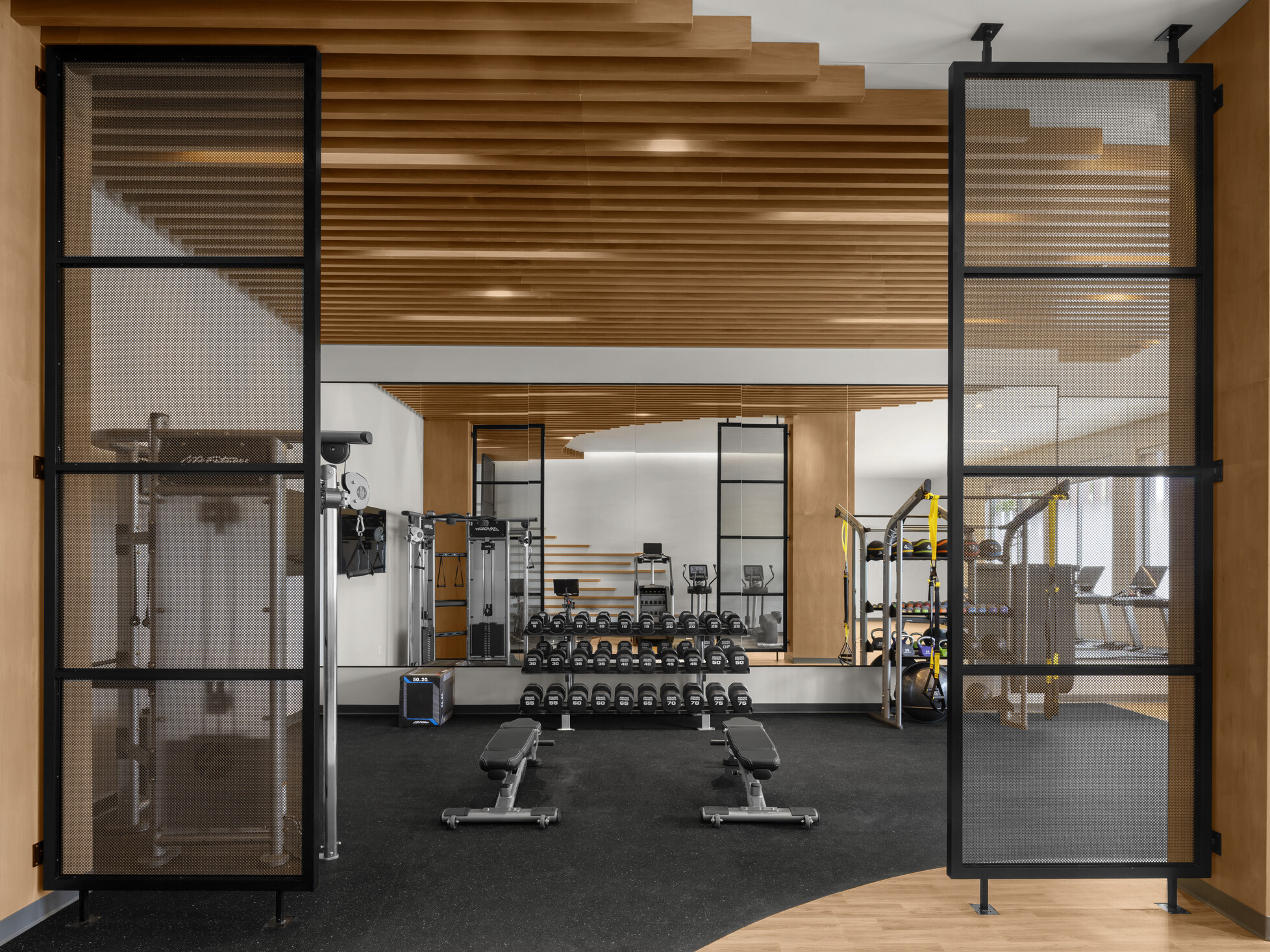 Fitness center at Hilton Jacksonville featuring honey-toned millwork, black metal accent screens at the entry, slat wood ceiling, and mixed wood and matte black performance flooring