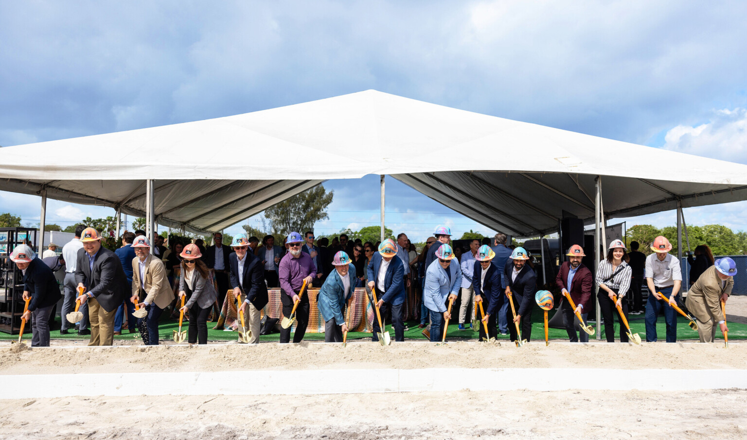 Multiple people in hard hats under a white tent holding shovels for a groundbreaking Multiple people in hard hats under a white tent holding shovels for a groundbreaking