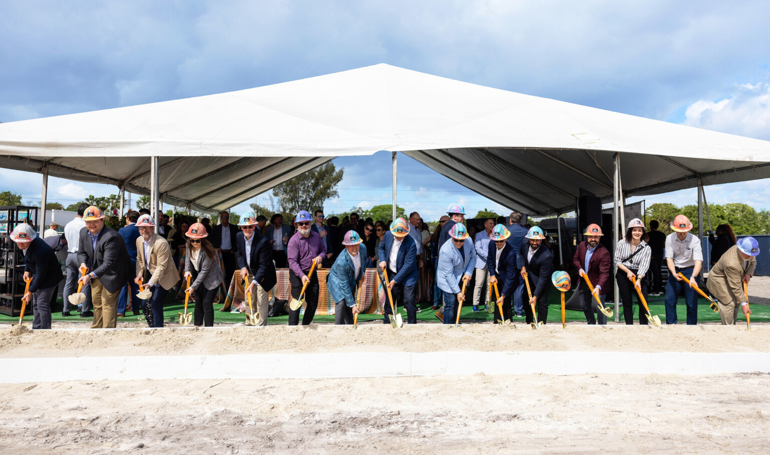 Multiple people in hard hats under a white tent holding shovels for a groundbreaking for T3 FAT Village