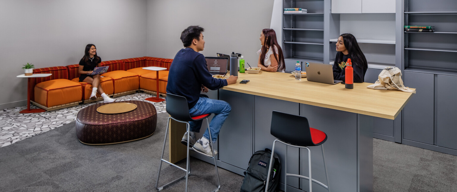 Students working in a lounge with grey cabinetry and a orange seating area