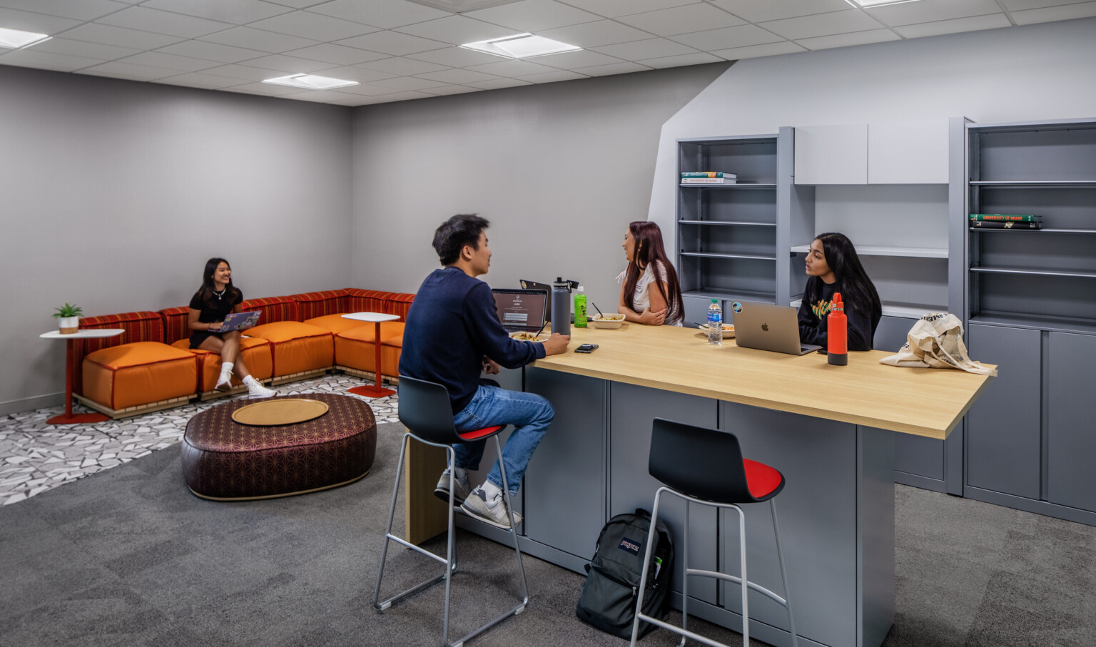 Students working in a lounge with grey cabinetry and a orange seating area