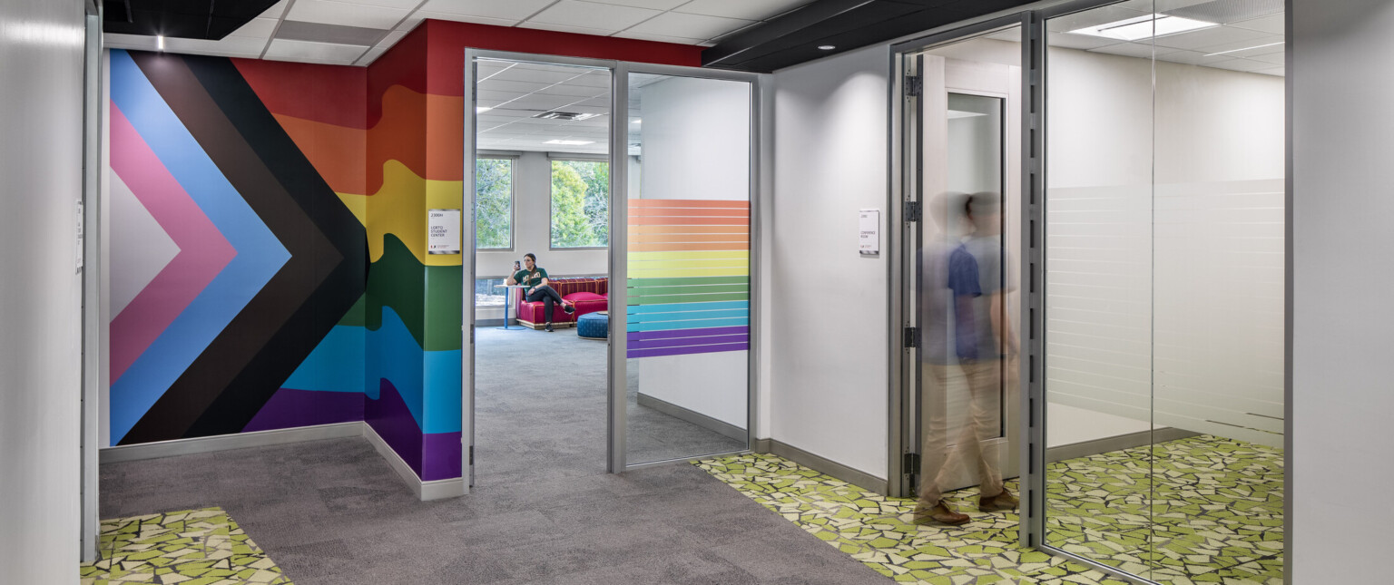 Hallway surrounded by glass offices with colorful murals on the walls and green flooring