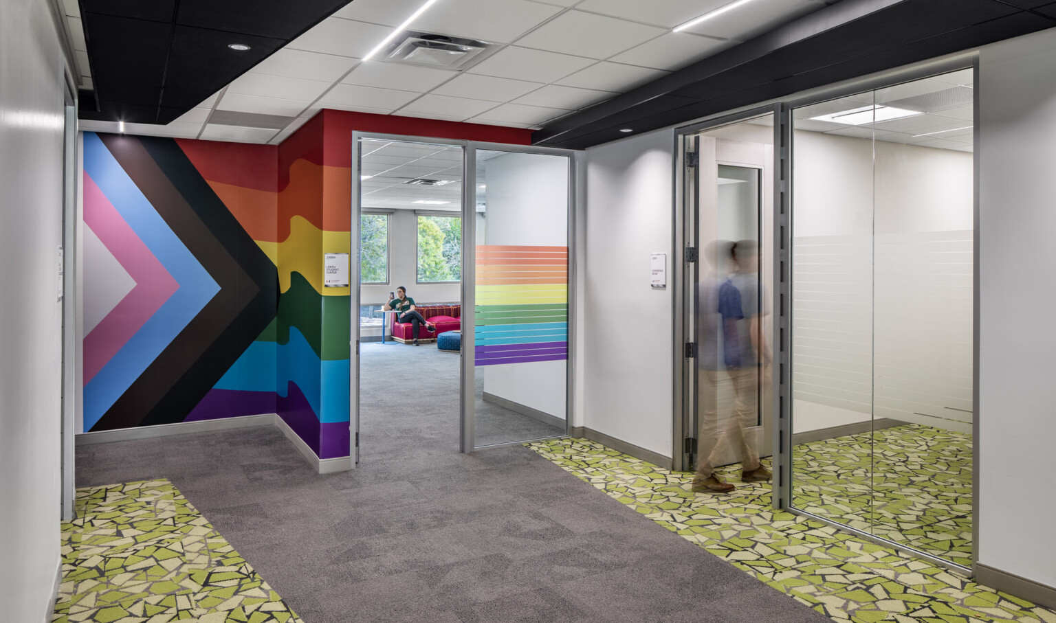 Hallway surrounded by glass offices with colorful murals on the walls and green flooring