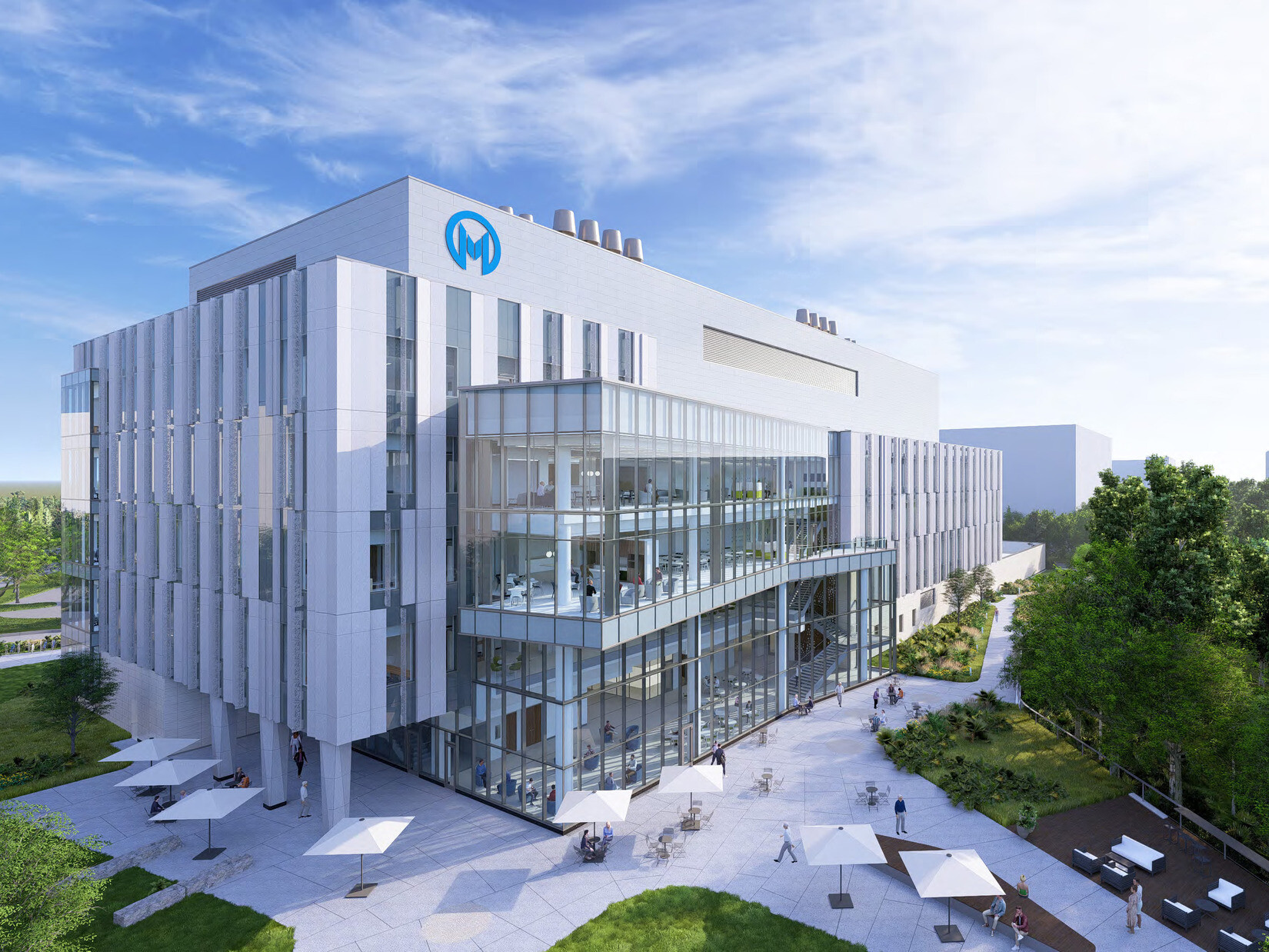 A modern, multi-story medical building with a glass façade and a logo featuring the letter 'M' on the top left corner. The building is surrounded by greenery and an outdoor courtyard with white umbrella-covered seating areas. People are walking and sitting in the courtyard.