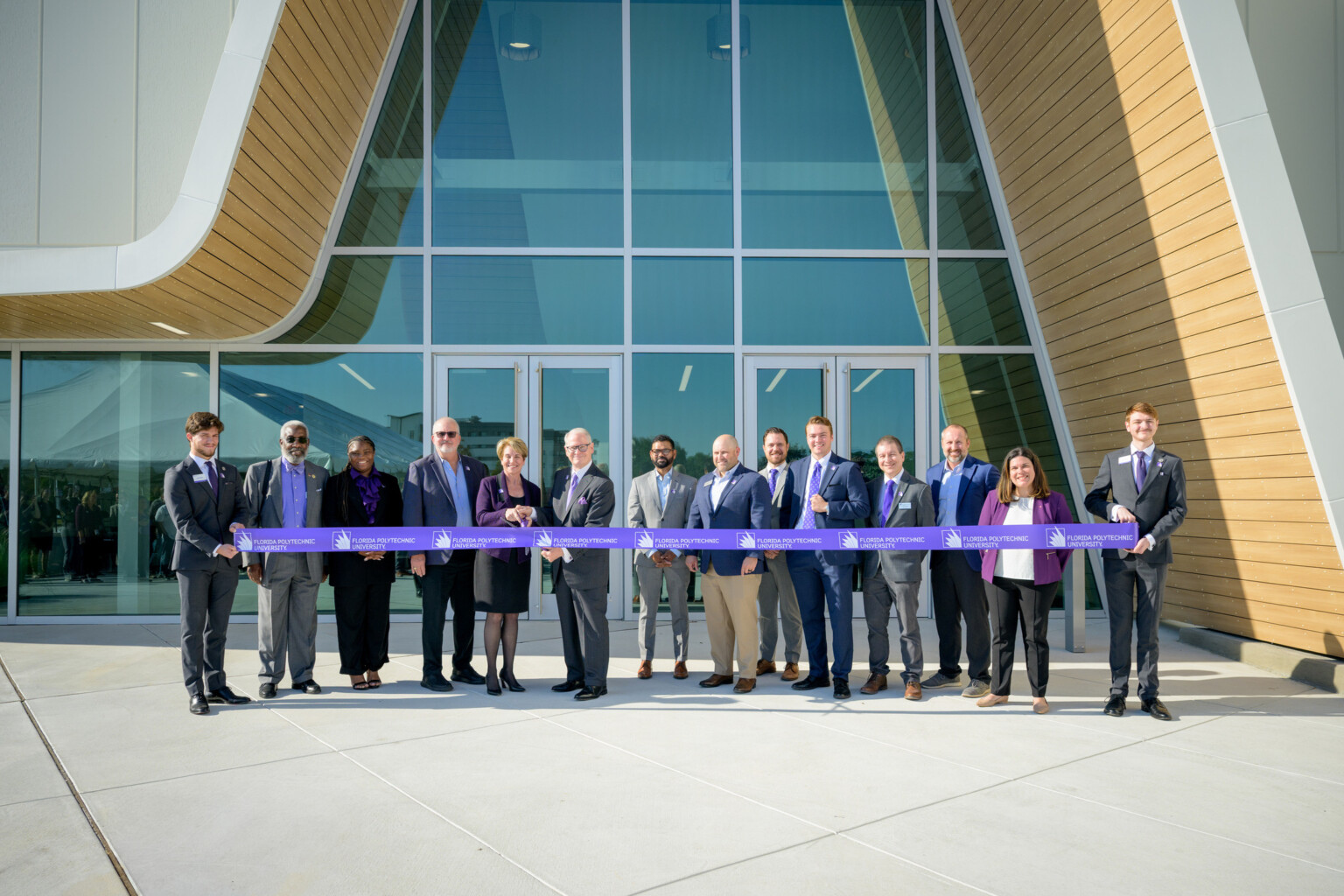professionals standing in front of modern asymmetrical building; line of people holding ribbon and cutting for ceremonial opening