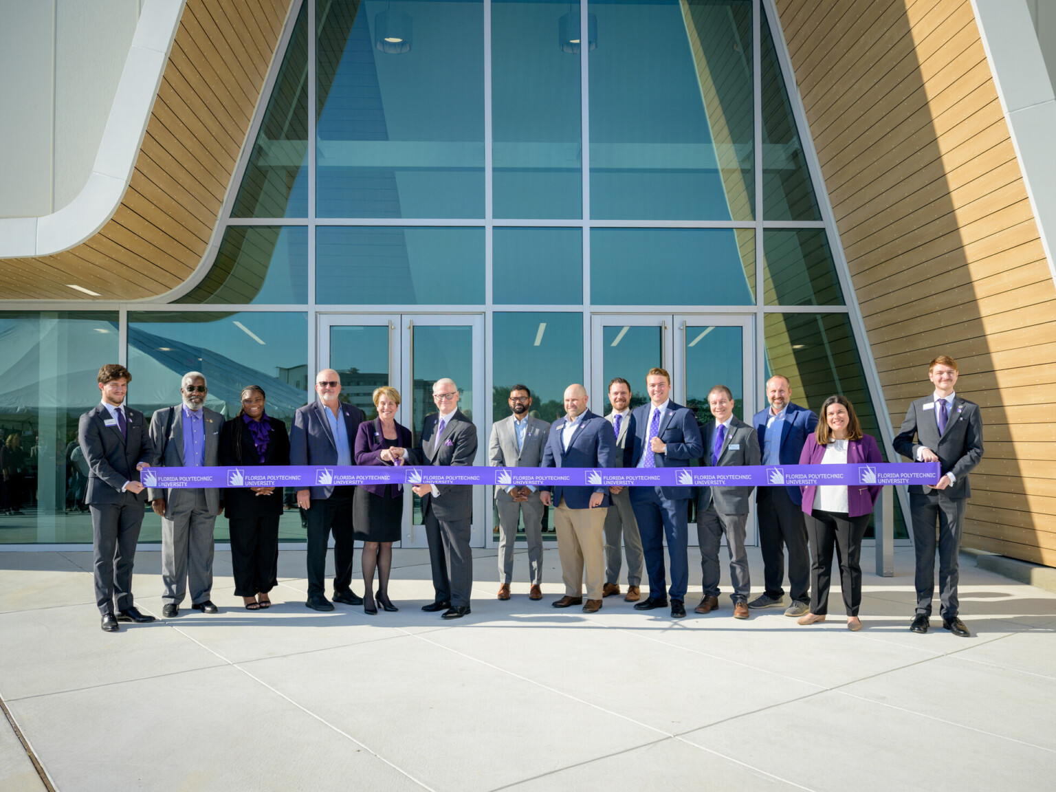 professionals standing in front of modern asymmetrical building; line of people holding ribbon and cutting for ceremonial opening