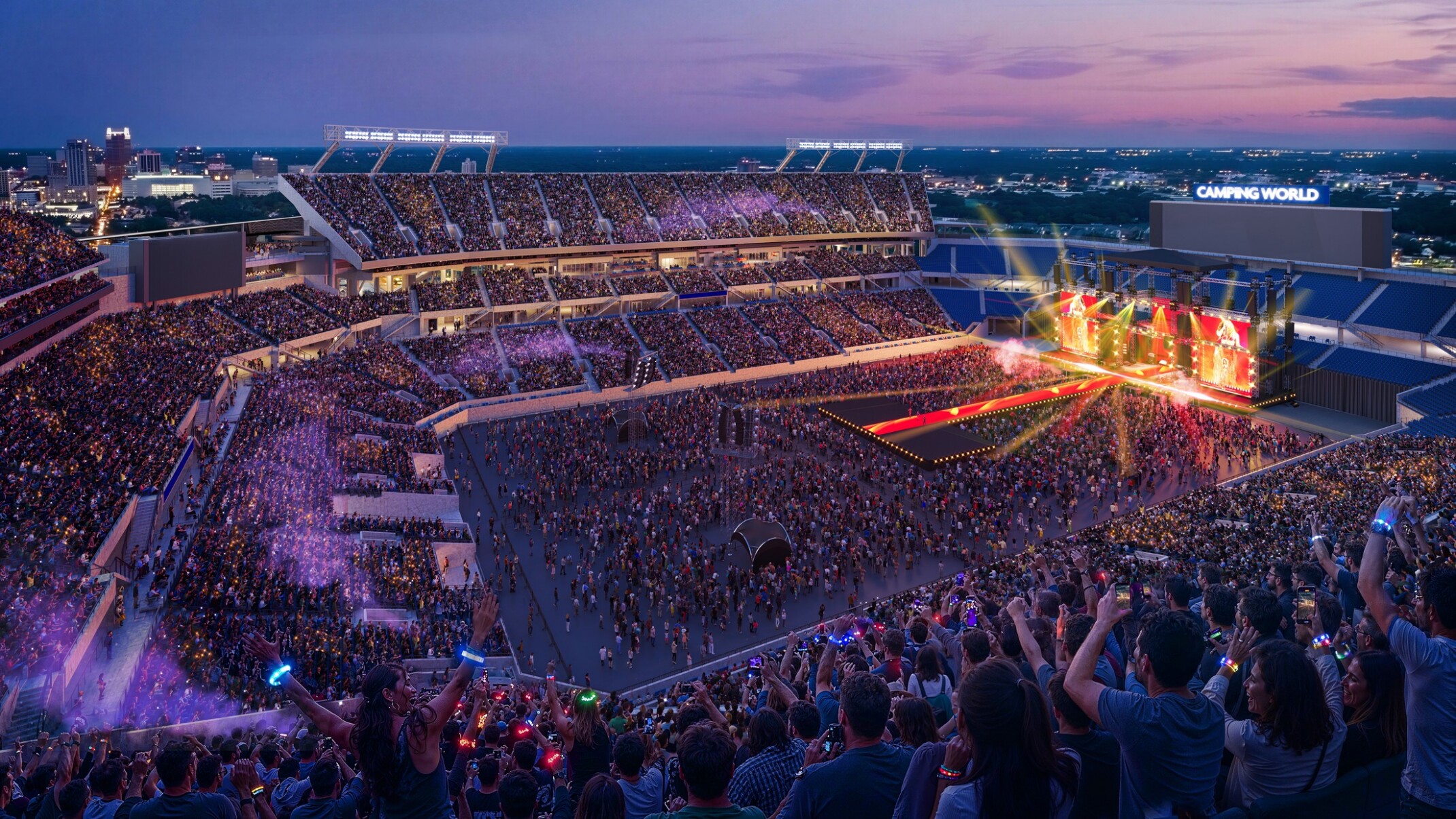 A wide view of a football stadium at sunset set up for a large concert, with a brightly lit stage on one end of the field featuring colorful lights and screen panels.