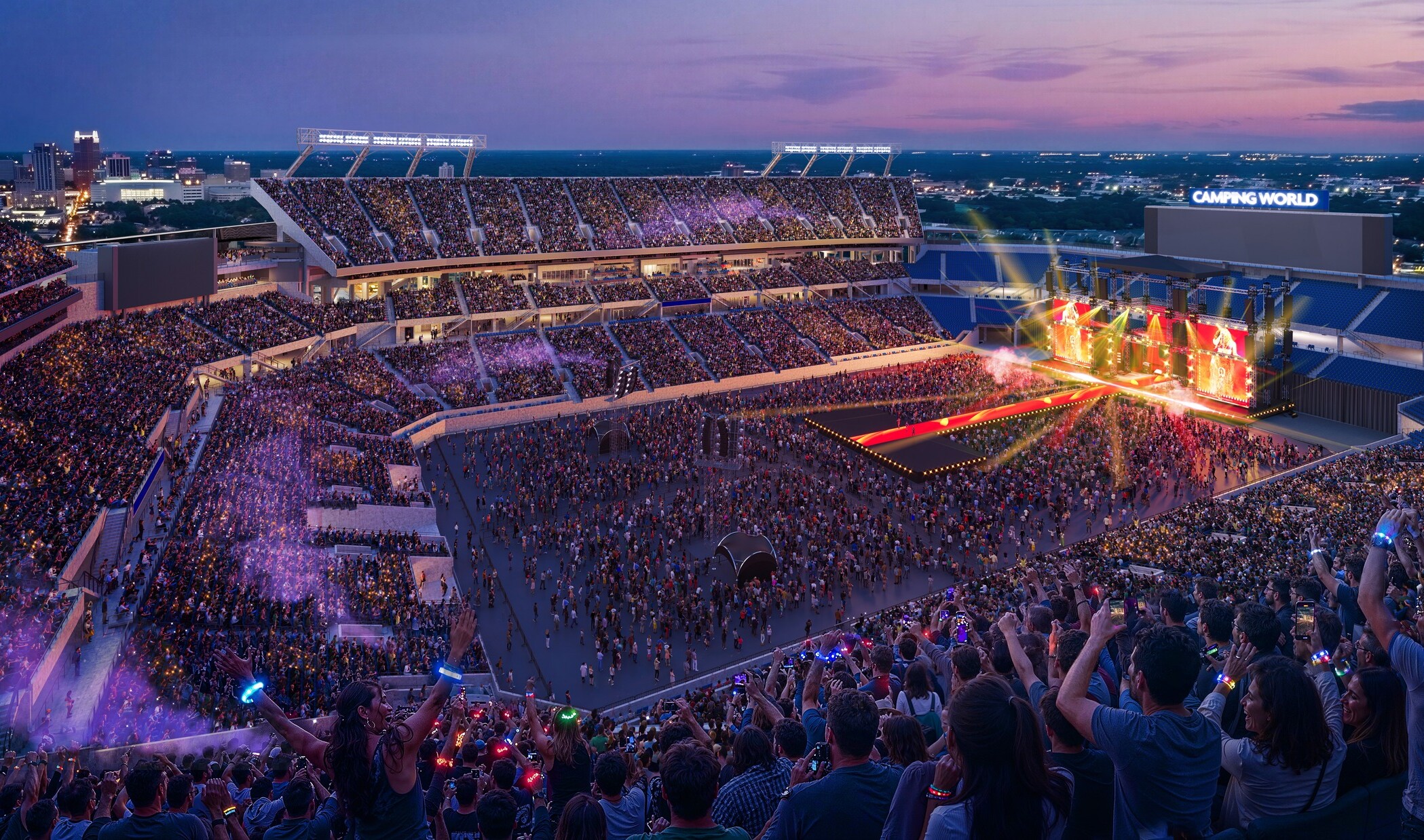 A wide view of a football stadium at sunset set up for a large concert, with a brightly lit stage on one end of the field featuring colorful lights and screen panels.