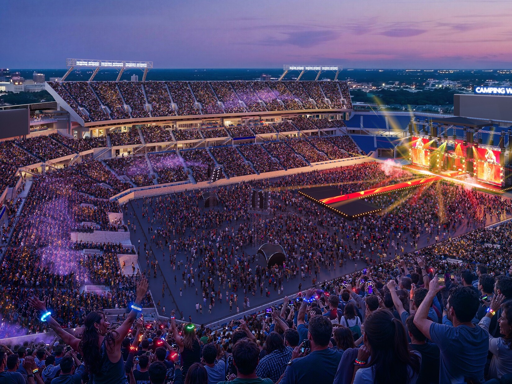 A wide view of a football stadium at sunset set up for a large concert, with a brightly lit stage on one end of the field featuring colorful lights and screen panels.