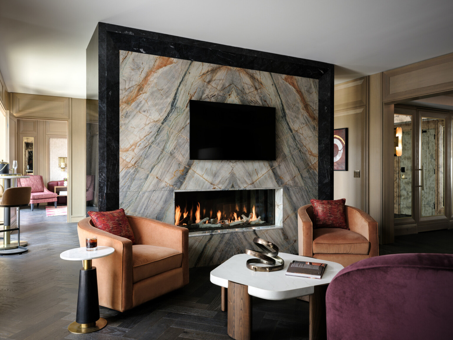 Marble fireplace with TV above separating a space with modern orange and purple furnishings on one side with bar stools and high tables on the other Marble fireplace with TV above separating a space with modern orange and purple furnishings on one side with bar stools and high tables on the other