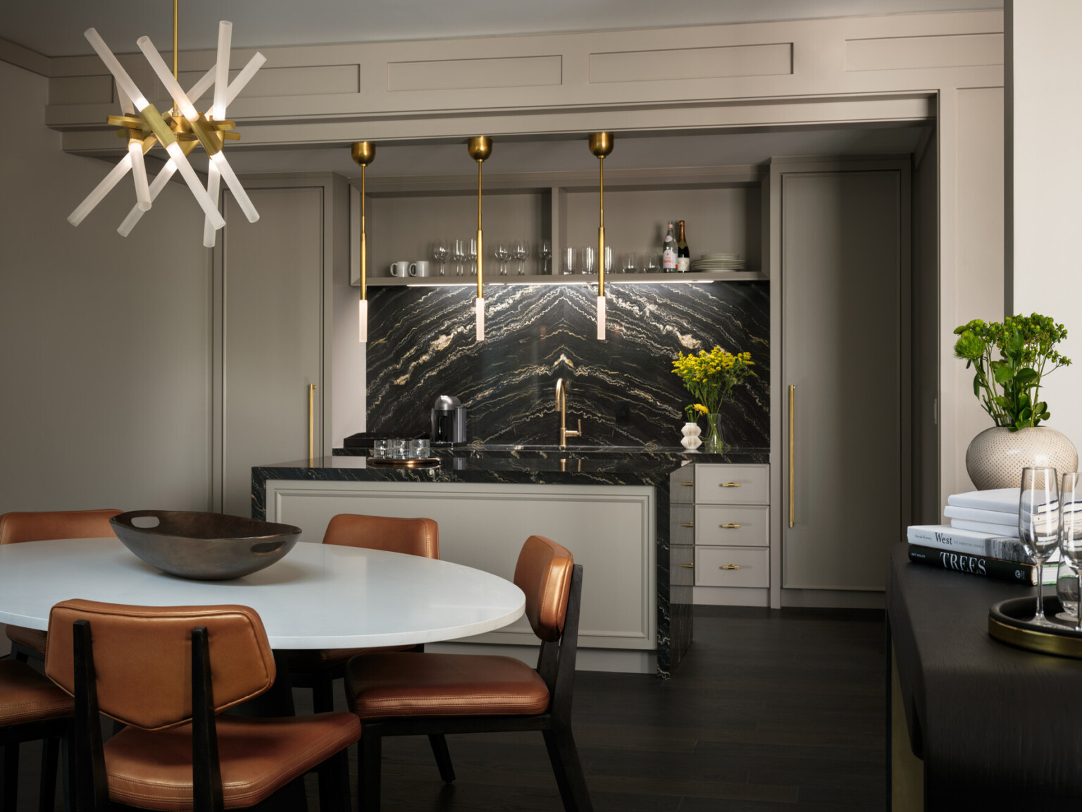 Seating area with white table and copper colored chairs in front of a island with black marble backsplash and counter with gold fixtures