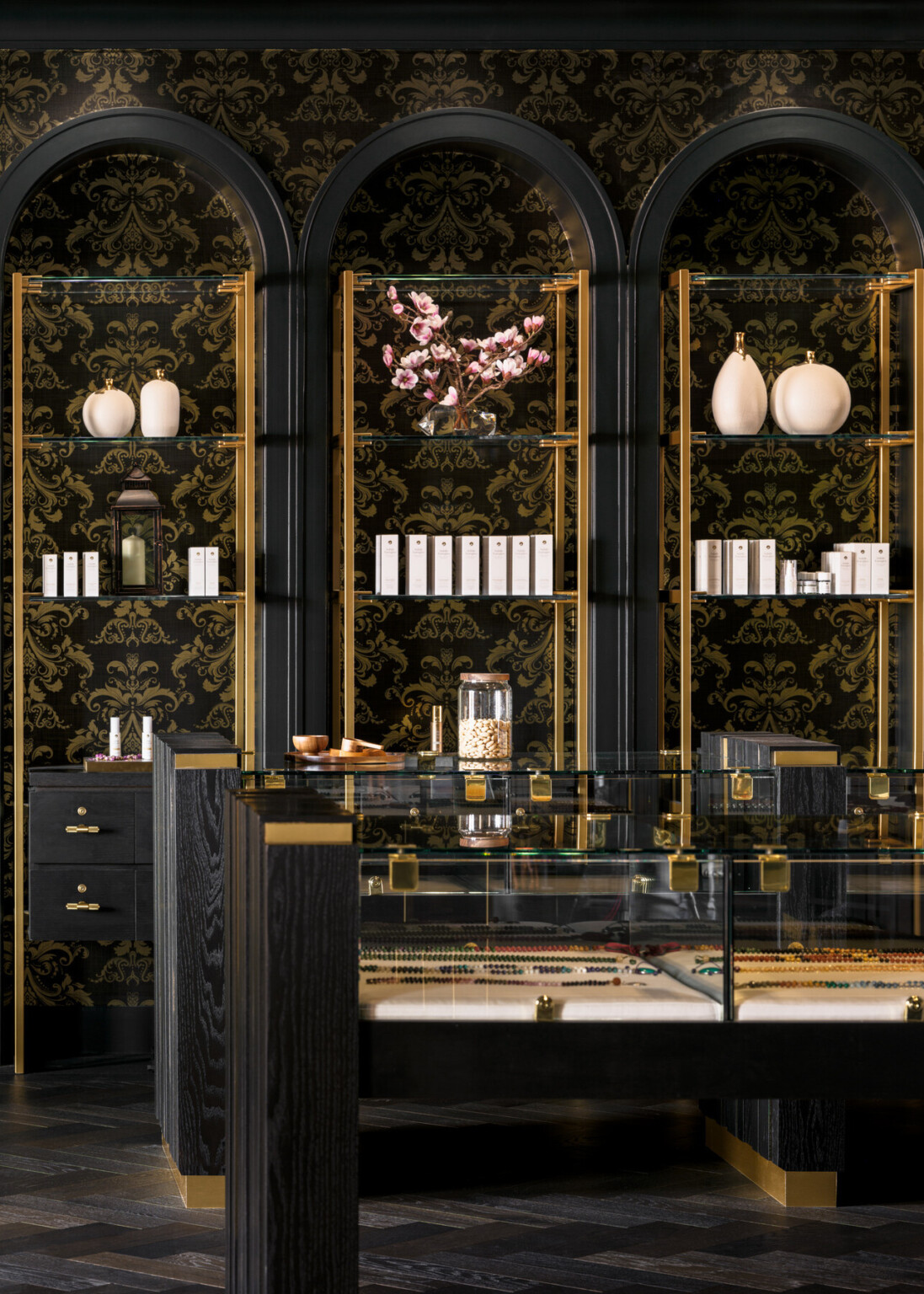 Black and gold shelves filled with objects, glass cases with black and gold accents, black flooring, black wallpaper with gold accents
